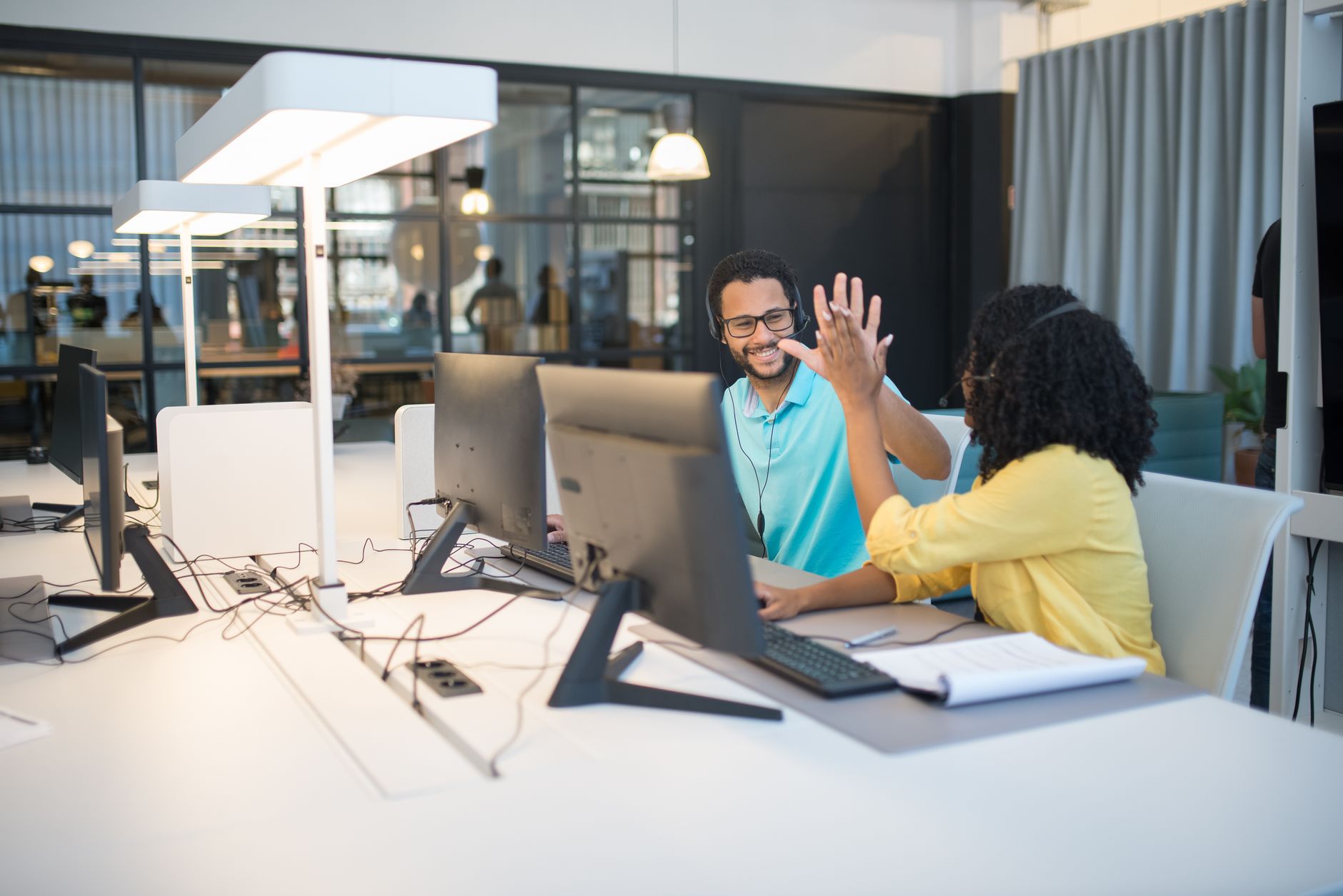 Two colleagues celebrate success with a high-five in a modern open-plan office environment.