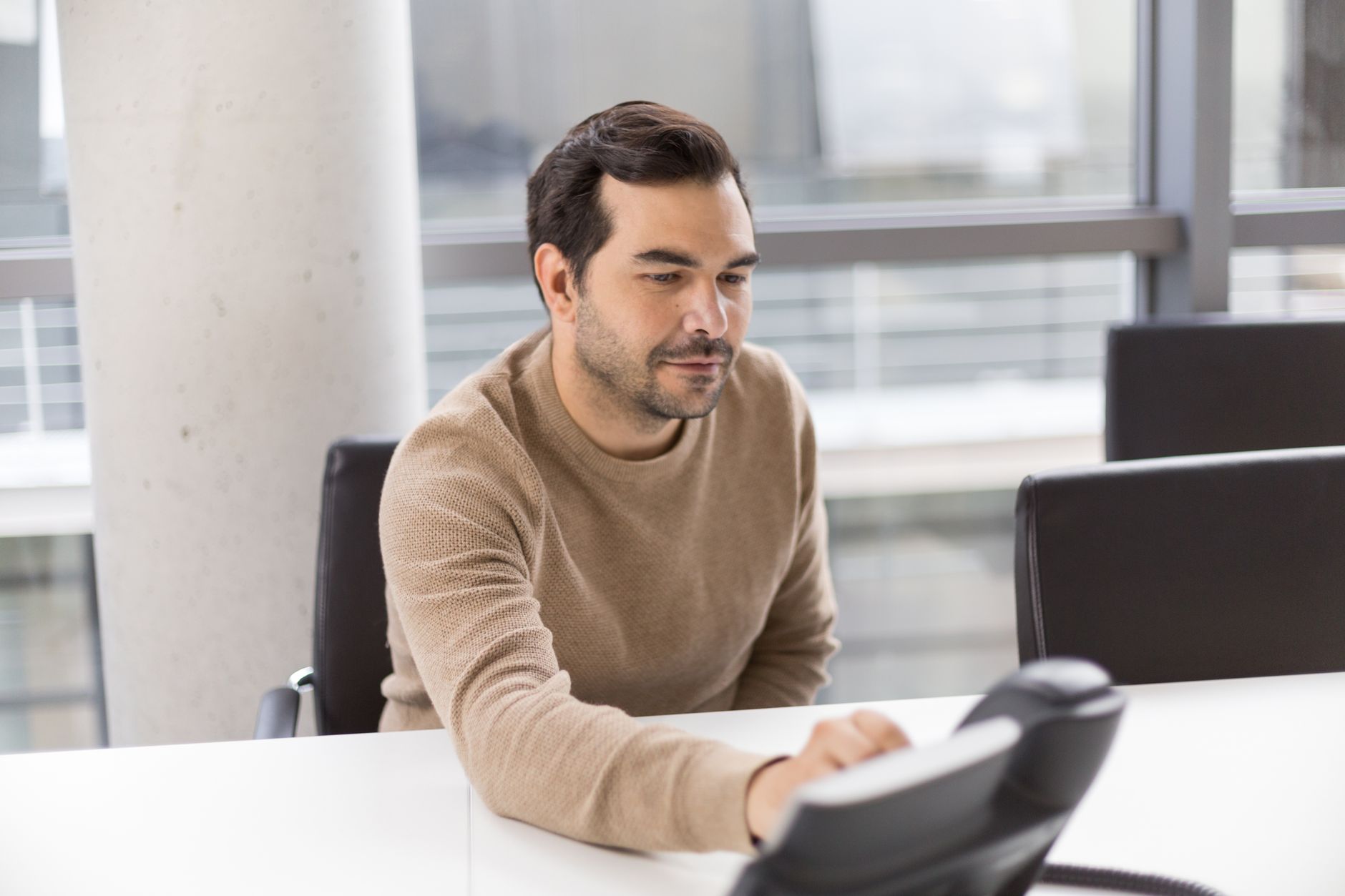 A man in a modern office working with a desk phone, showcasing a professional business environment.