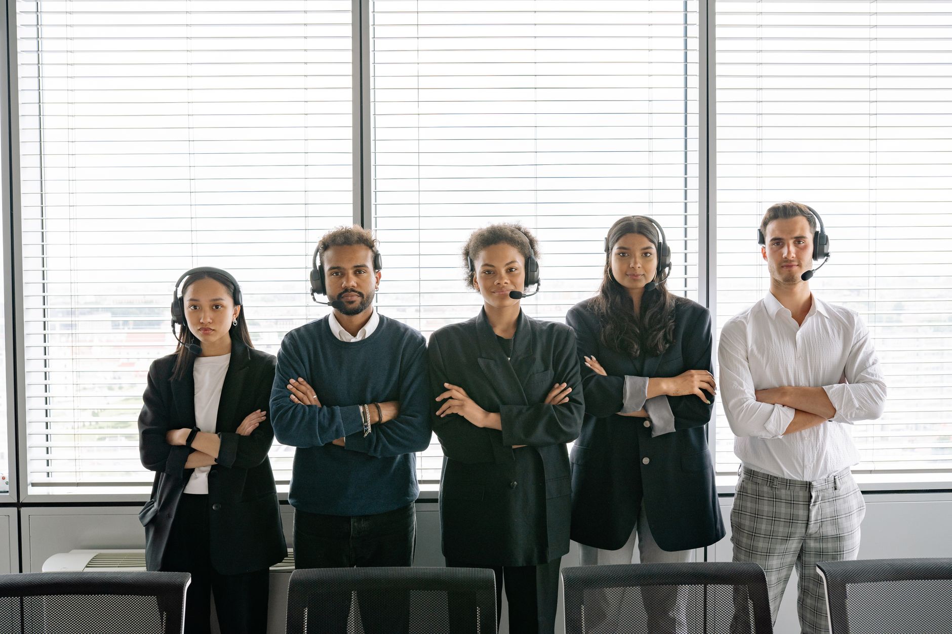 A diverse group of call center agents standing with arms crossed, wearing headsets in an office.