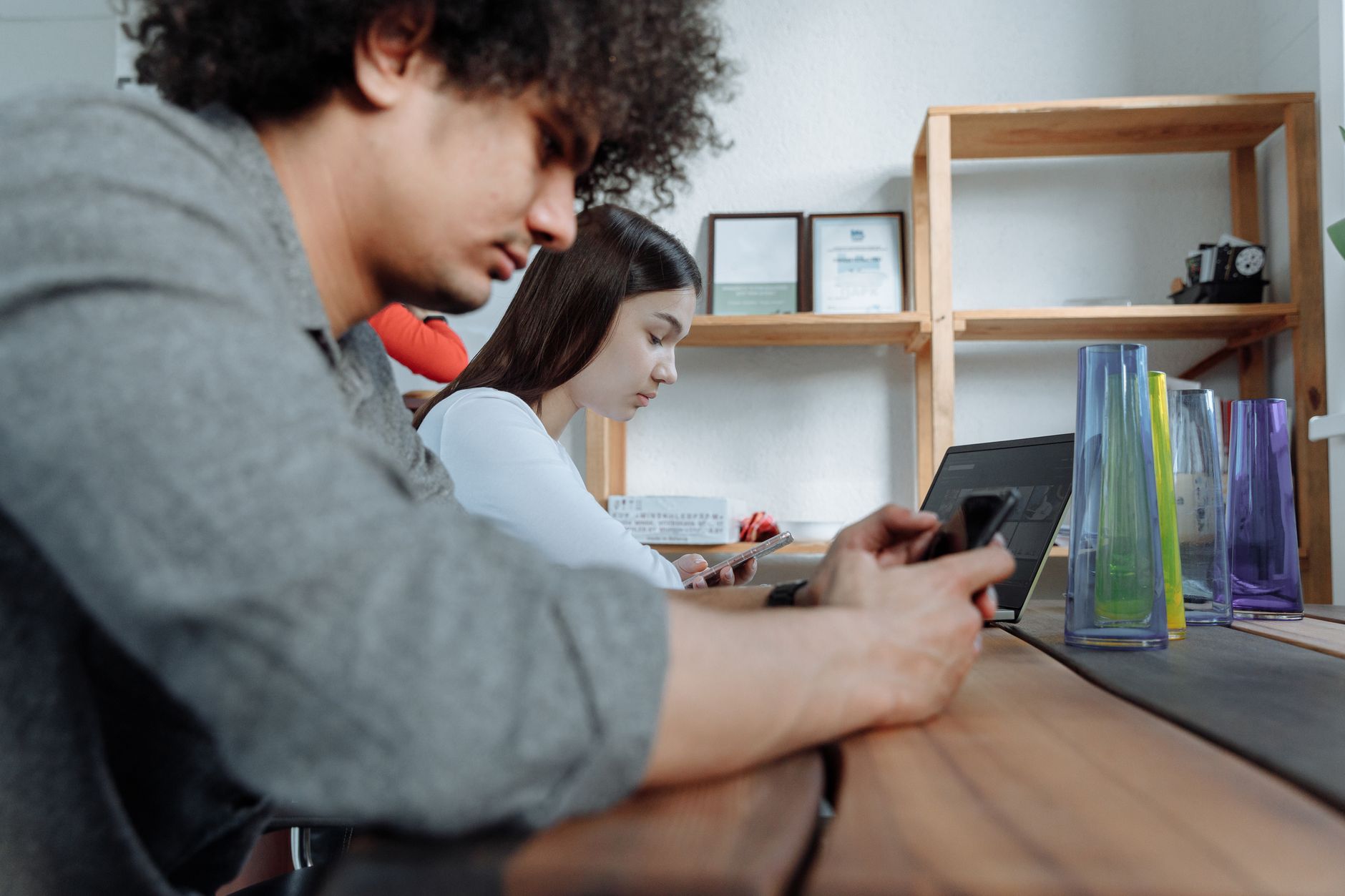 Students focused on smartphones and laptops in a modern classroom setting.