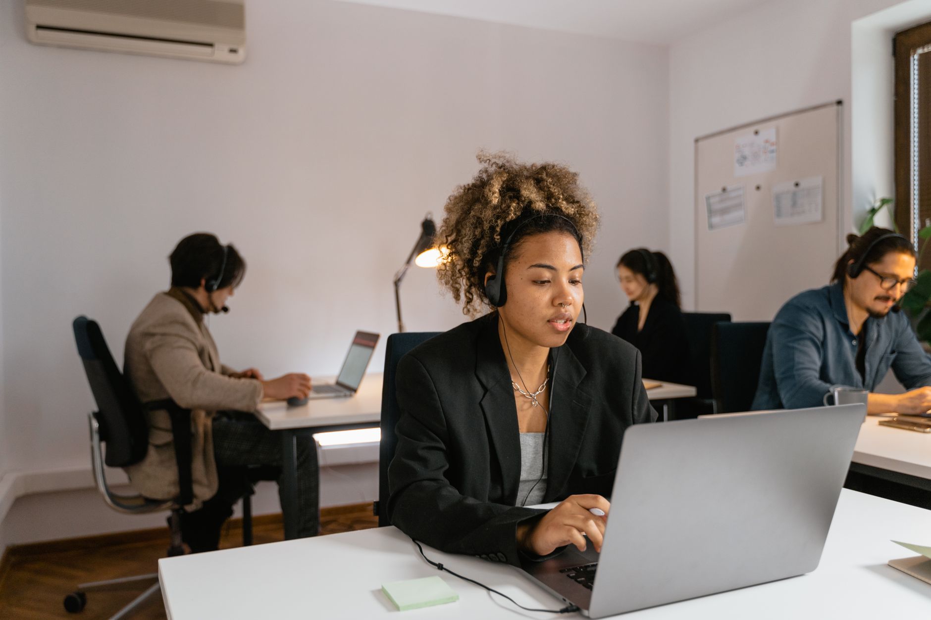 Professional team members with headsets working at laptops in a modern office setting.