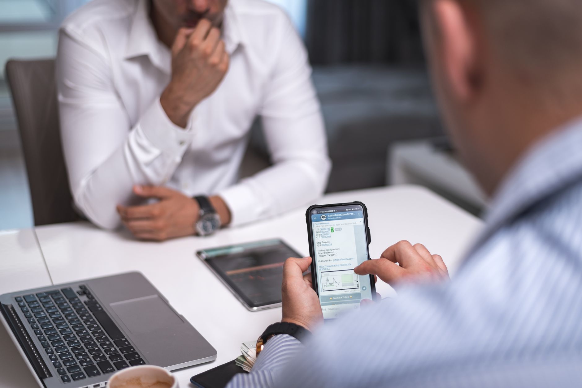 Two businessmen in a meeting room using a smartphone and laptop for a professional discussion.