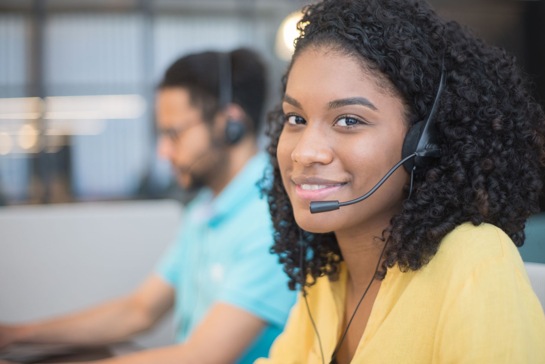 Professional woman with curly hair and headset smiling in a call center environment.