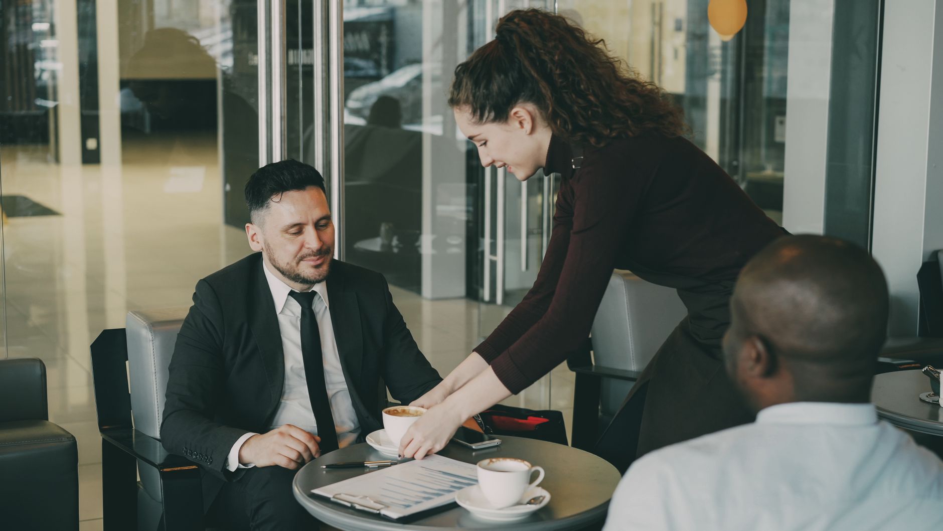 A business meeting in a café as waitress serves coffee to professionals.