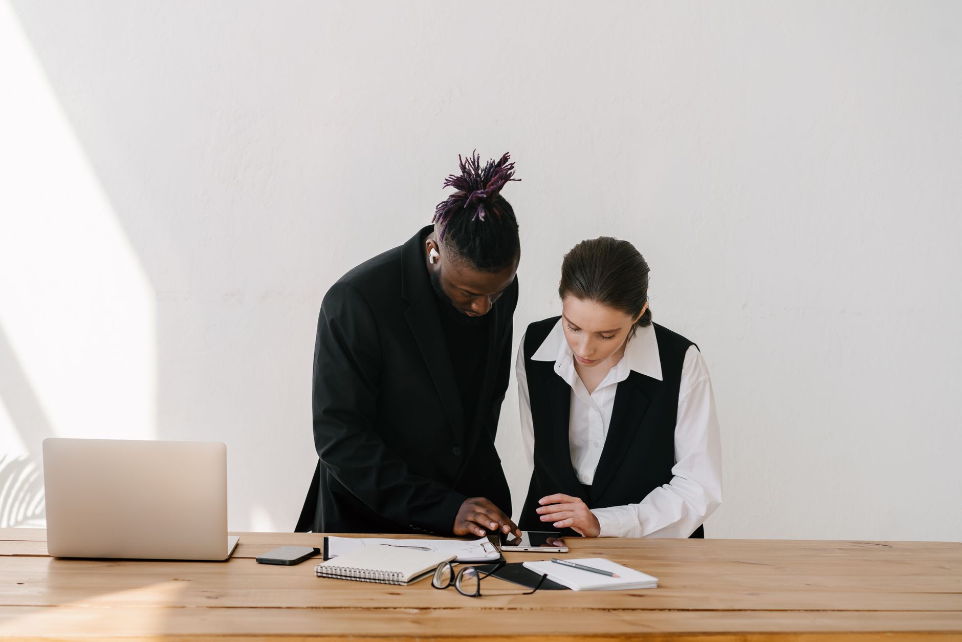Two colleagues working together at a wooden table in an office setting.
