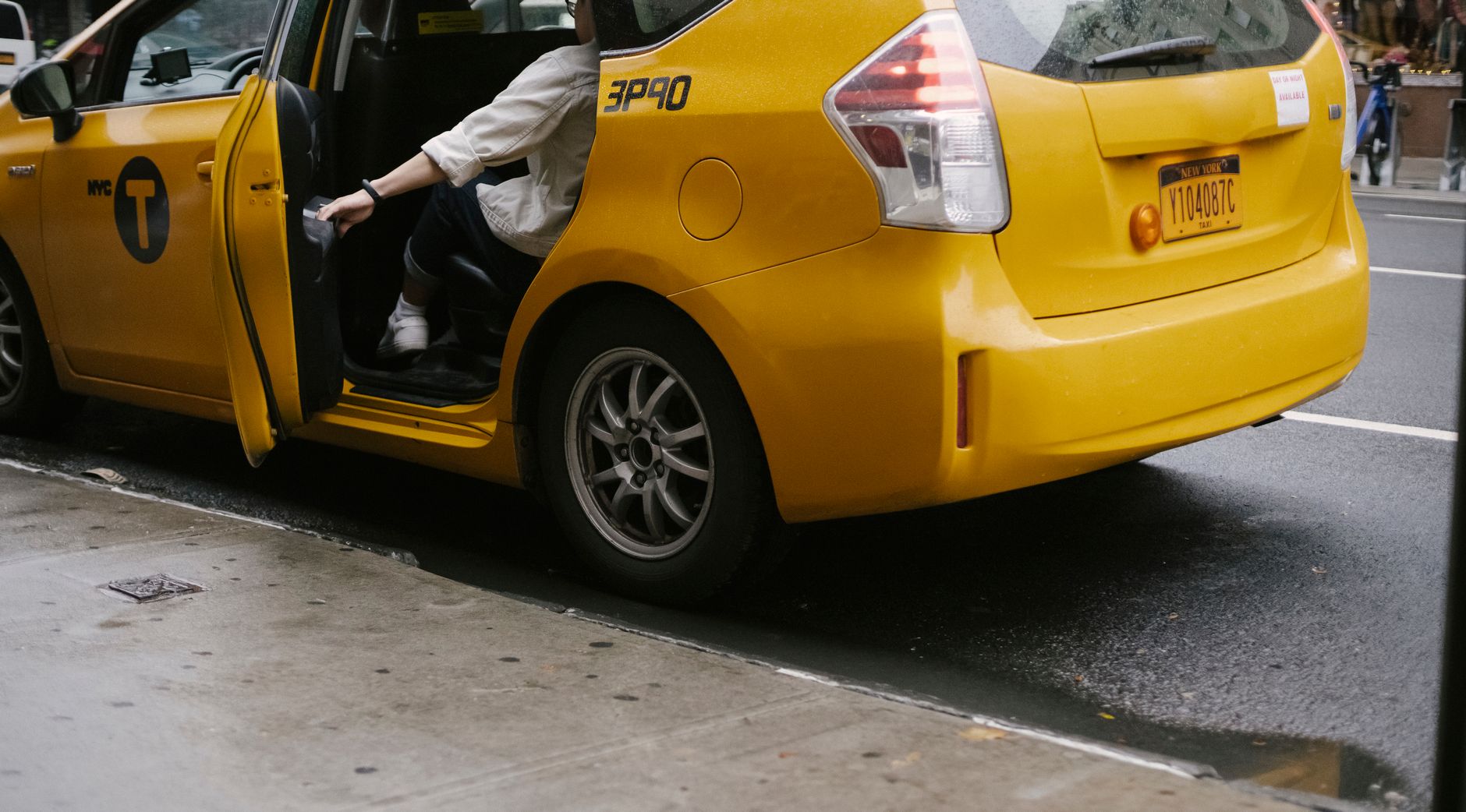 Unrecognizable passenger closing door of yellow cab with logo and headlight parked on asphalt road near pavement on street in city