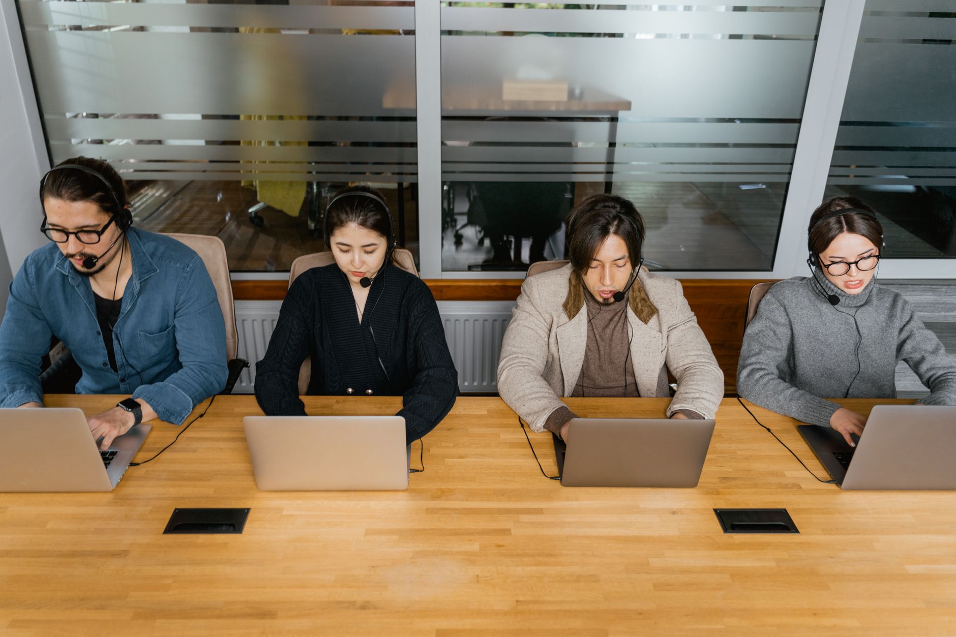 Group of diverse employees in headsets working on laptops in a modern office space.