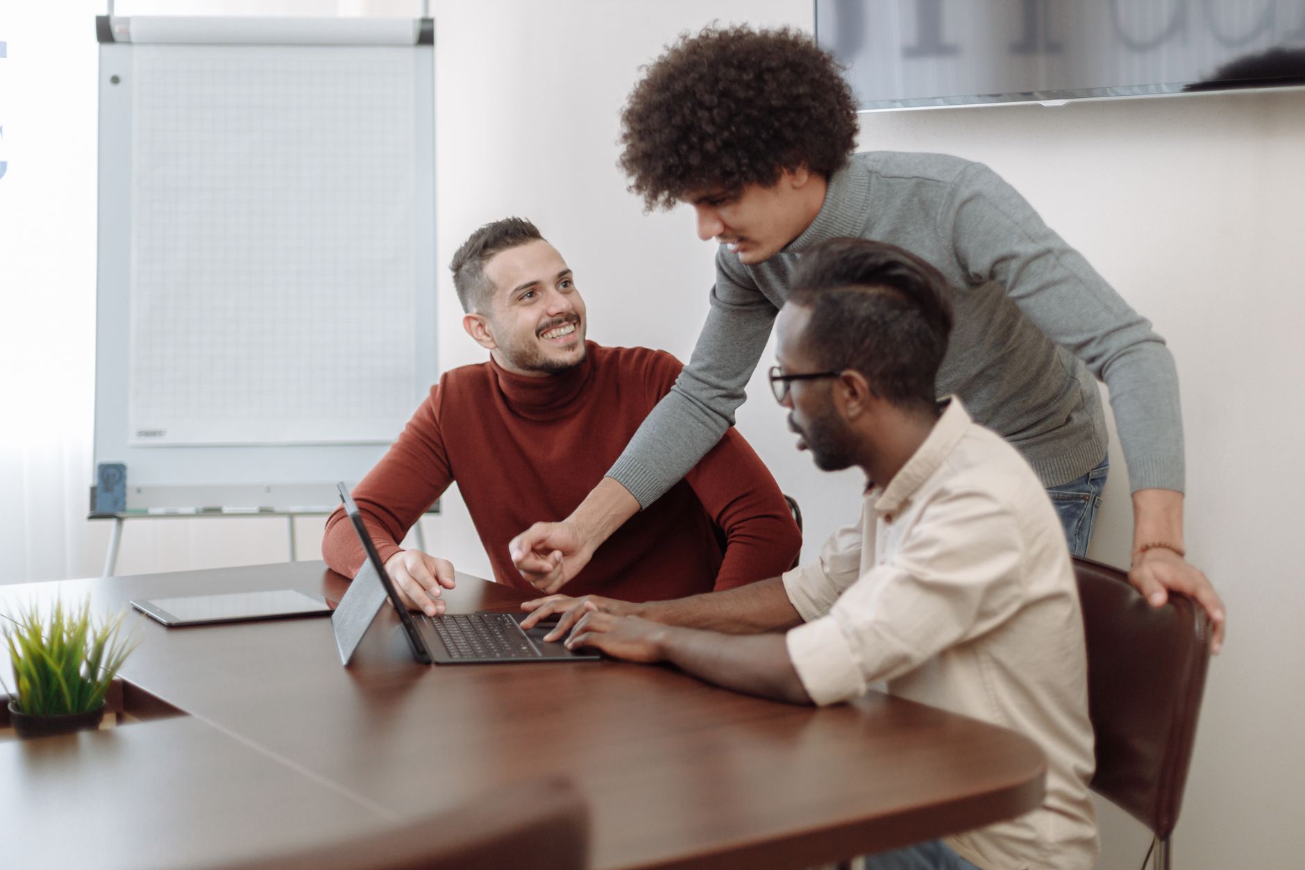 Three colleagues engaged in a collaborative meeting indoors, discussing project ideas around a laptop.