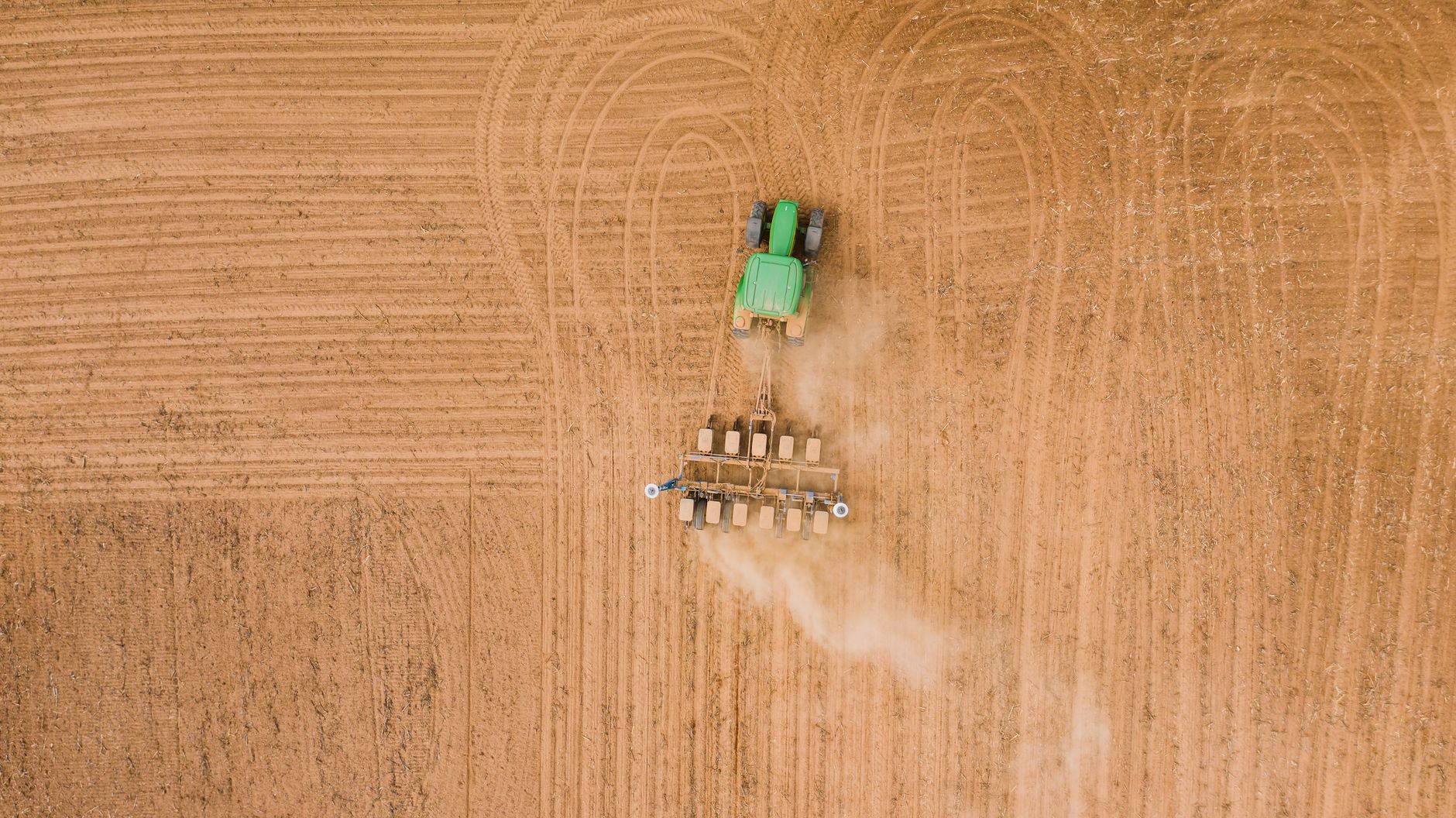 Drone view of modern tractor plowing beige plantation and leaving traces and haze