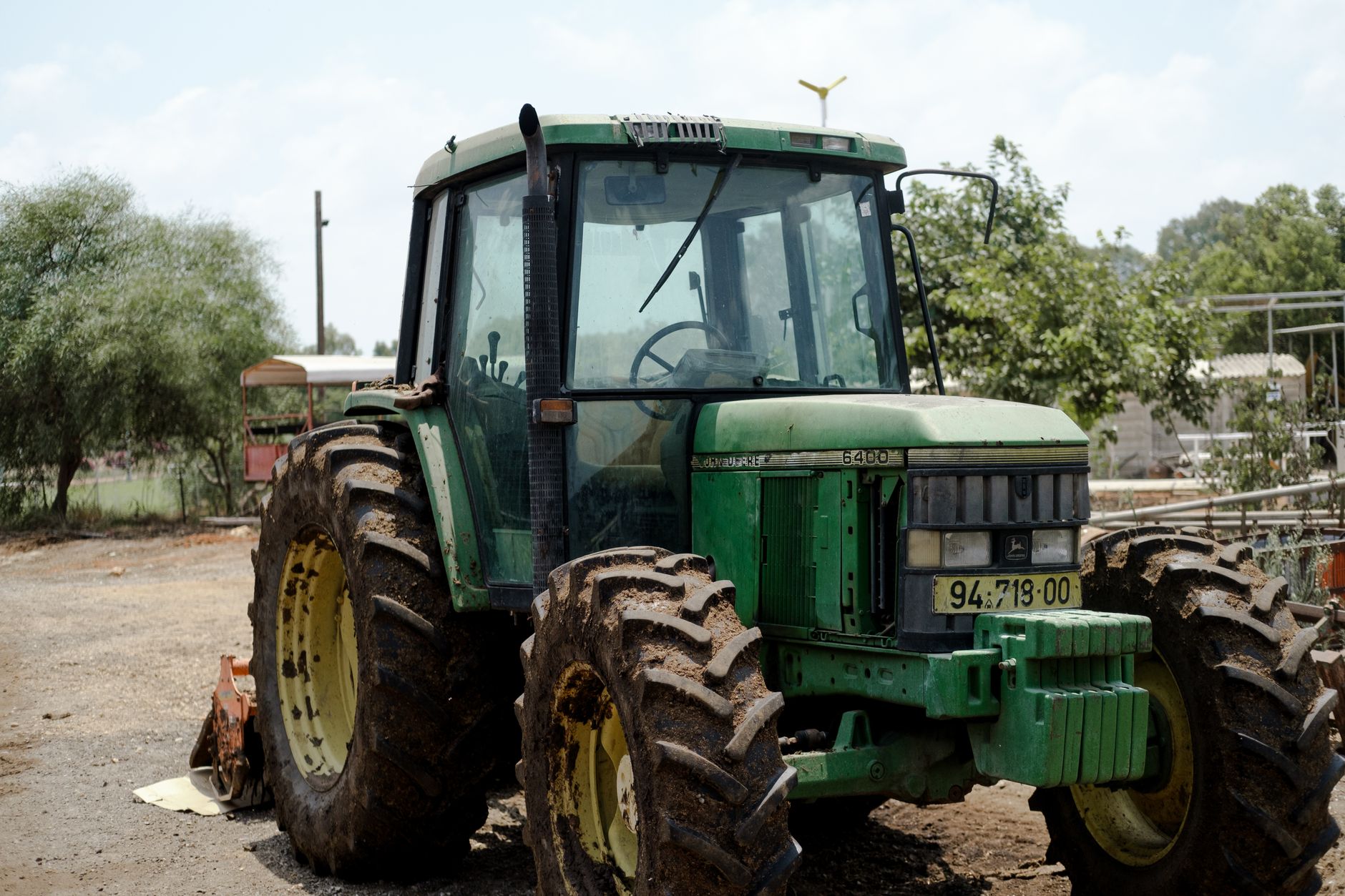 A robust John Deere tractor with muddy tires, parked on a sunny rural farm.