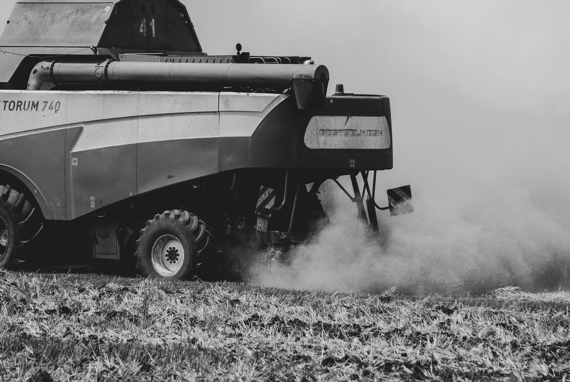 Monochrome image of a tractor on a field, creating dust clouds.