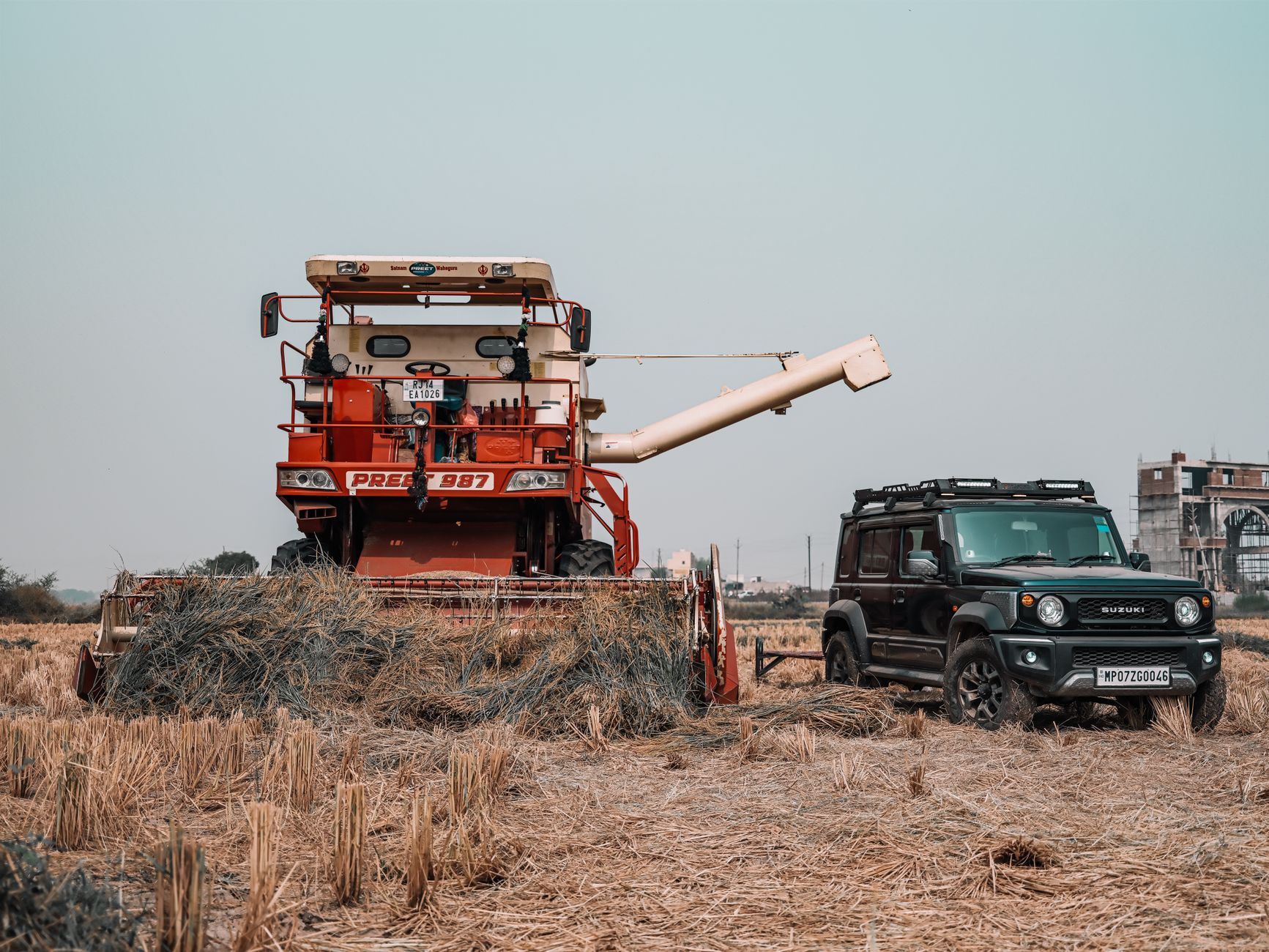 A black SUV and red combine harvester in a rural field during the day.