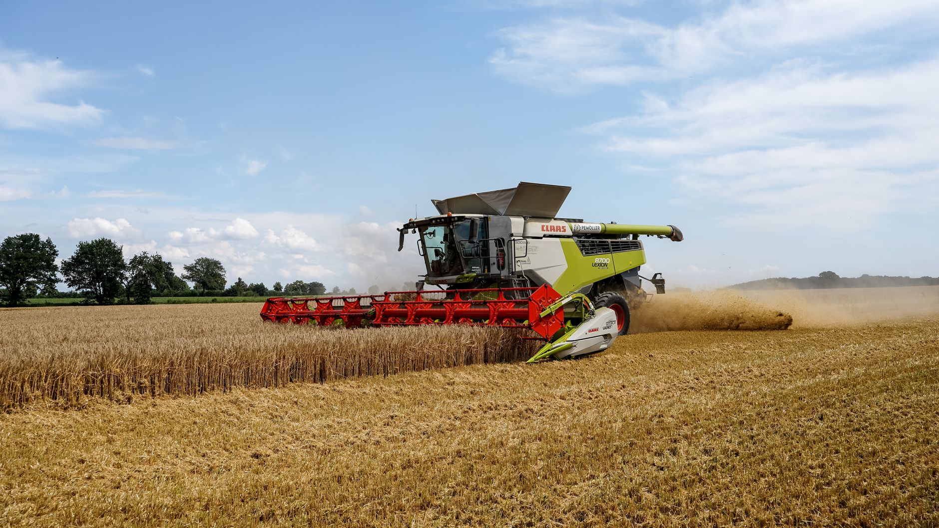 A Claas combine harvester operating in a golden wheat field under a bright summer sky in Germany.