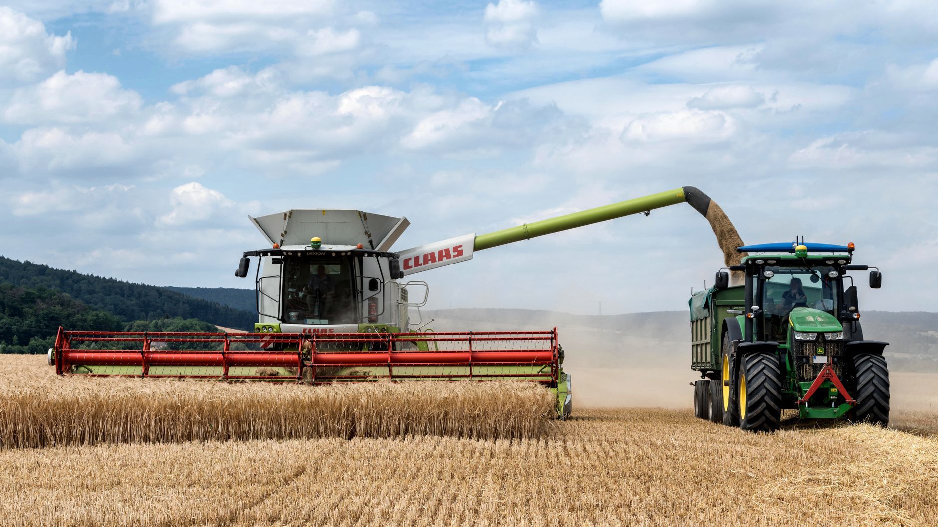 Combine harvester transferring wheat to tractor on a summer day in Paderborn.