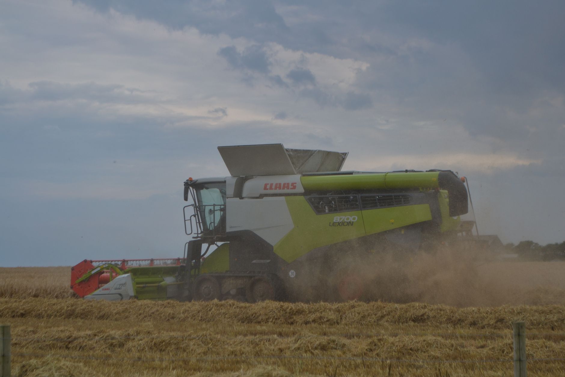 A green combine harvester efficiently working in a wheat field under a cloudy sky during dusk, capturing the essence of agriculture.