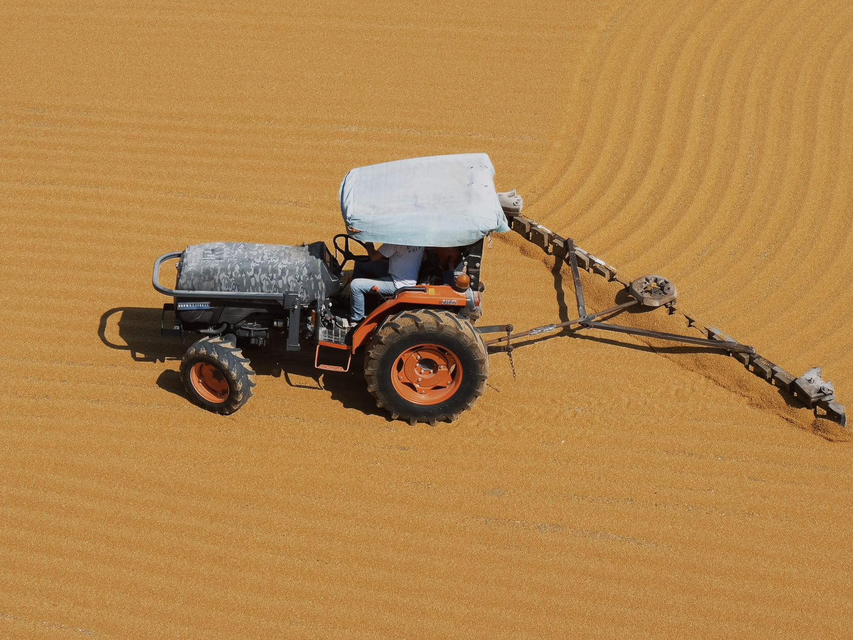 A tractor plows a sunlit field creating symmetrical patterns seen from above.