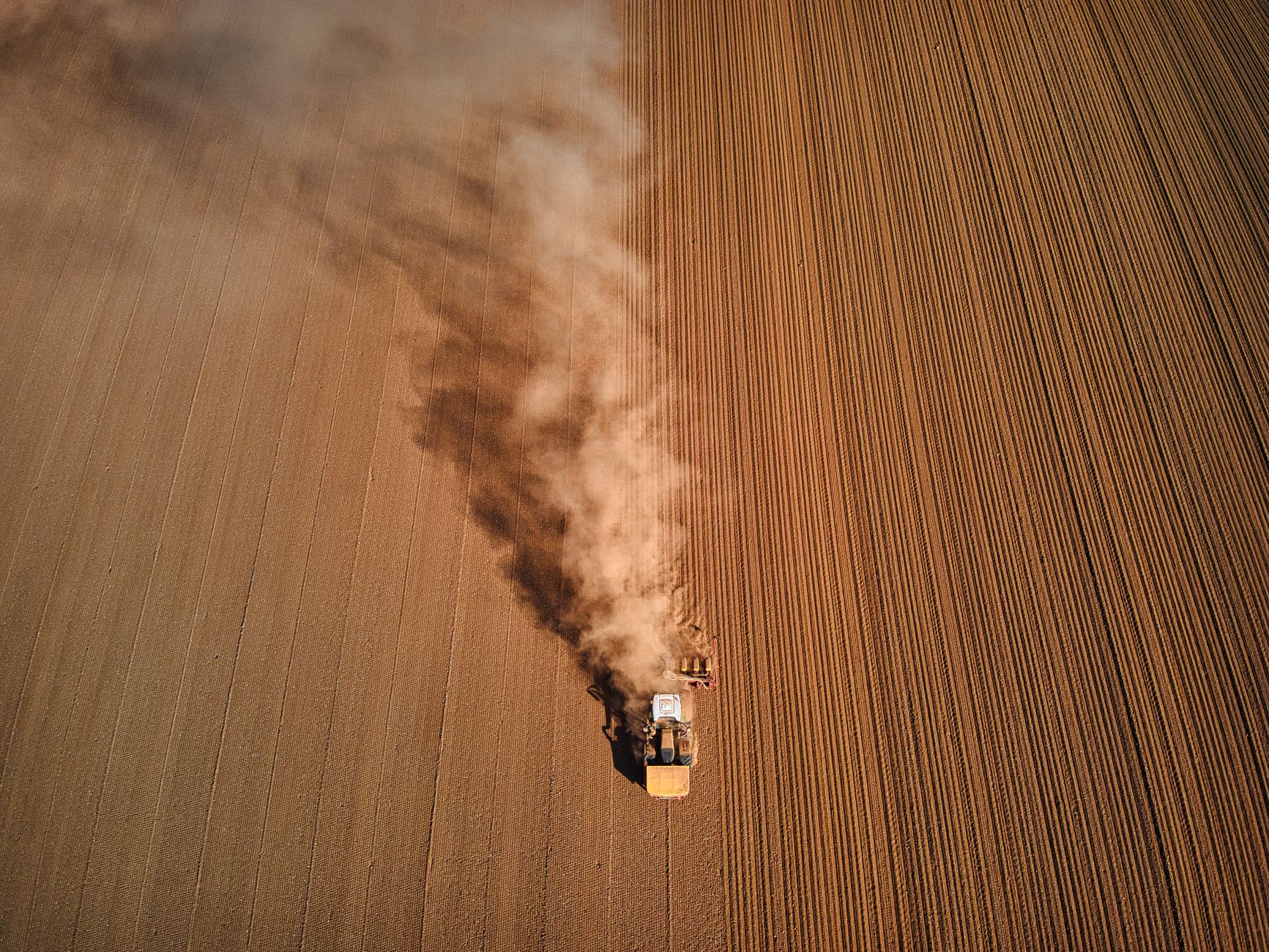 Aerial shot of a tractor ploughing a dusty field in High Peak, England, showcasing rural agriculture.