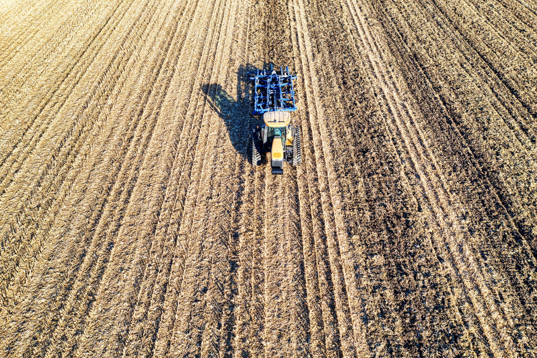 A drone captures a tractor plowing vast cropland under bright sunlight in Minnesota.