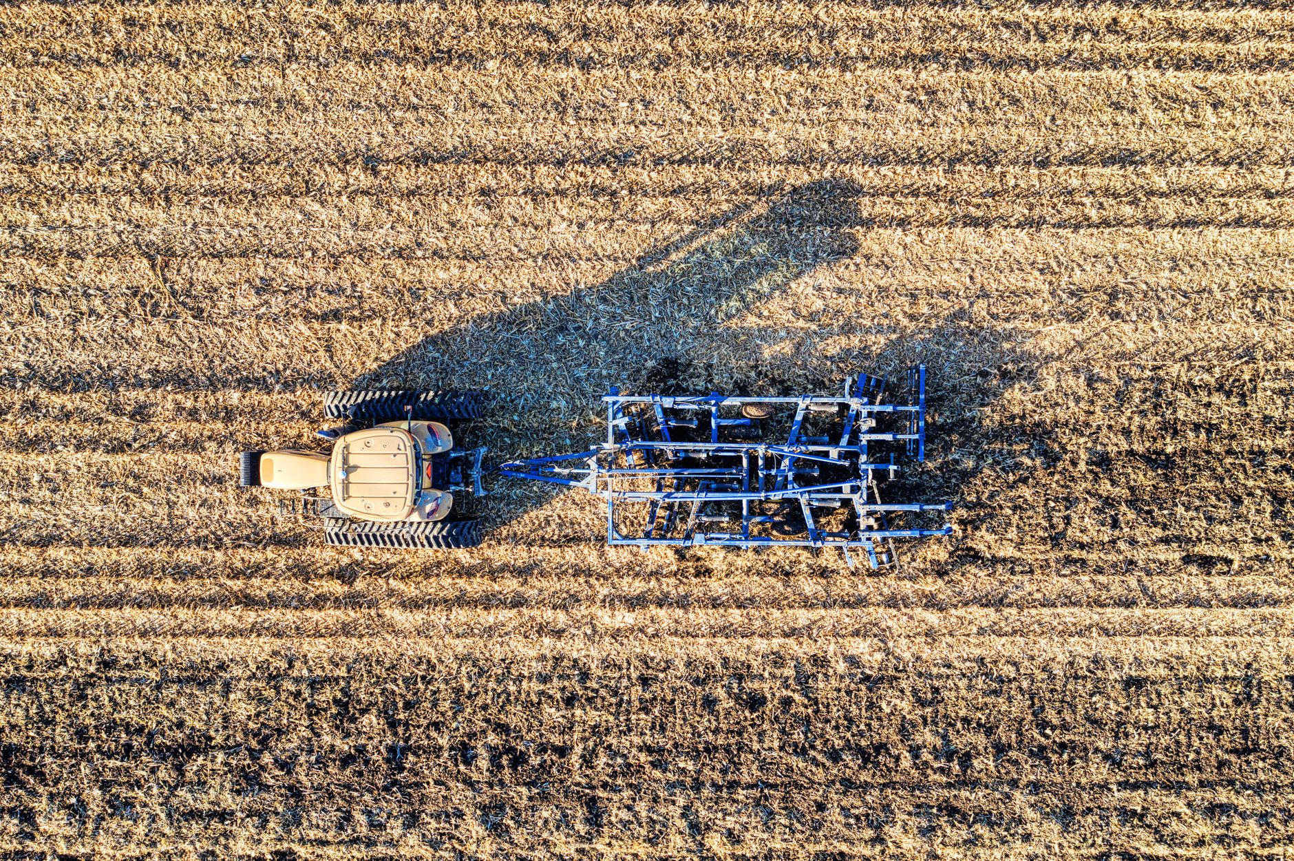 Drone shot of a tractor plowing a field in Minnesota during autumn showcasing modern farming techniques.
