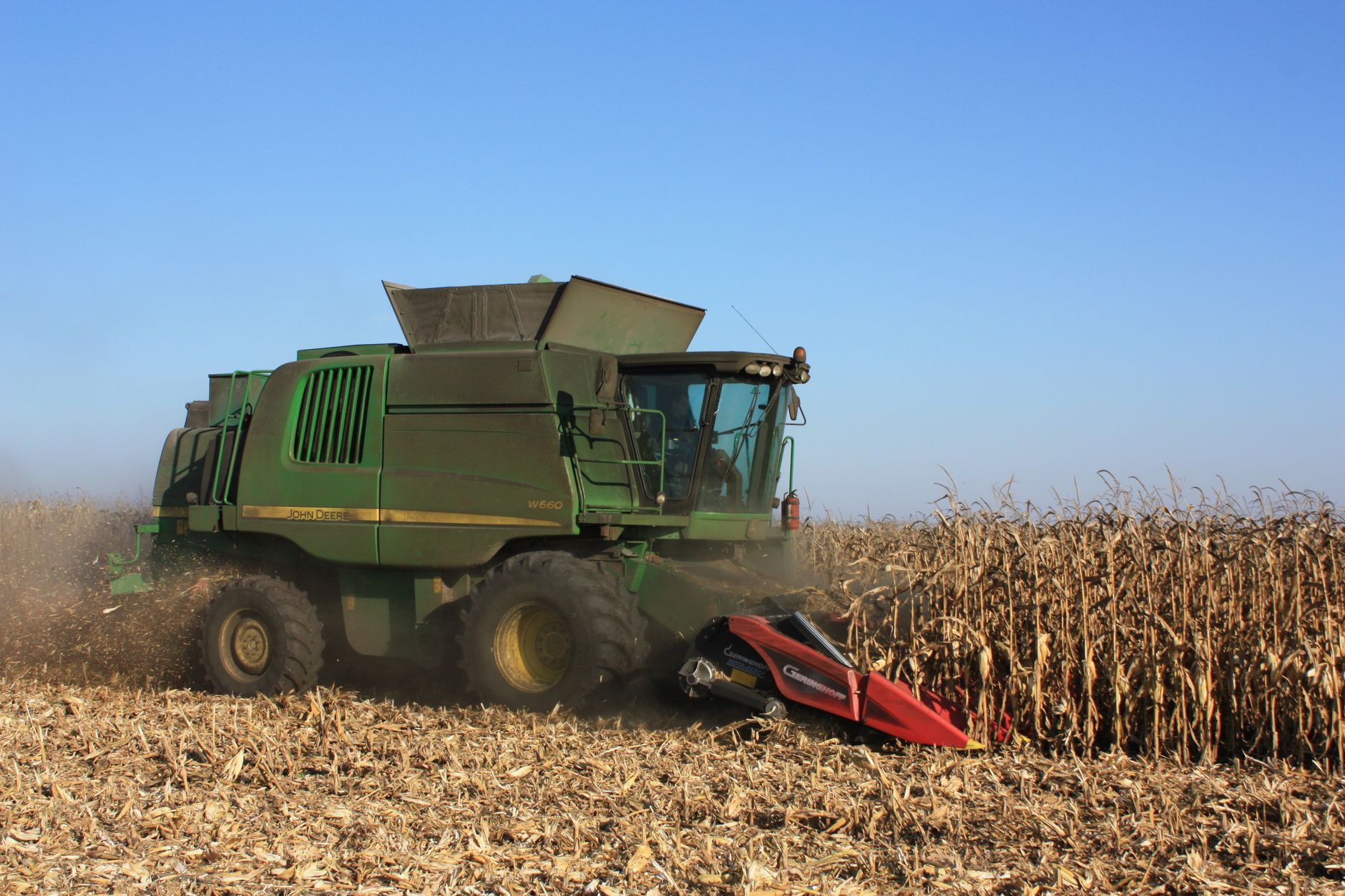 Combine harvester harvesting corn on a sunny day in a rural field.