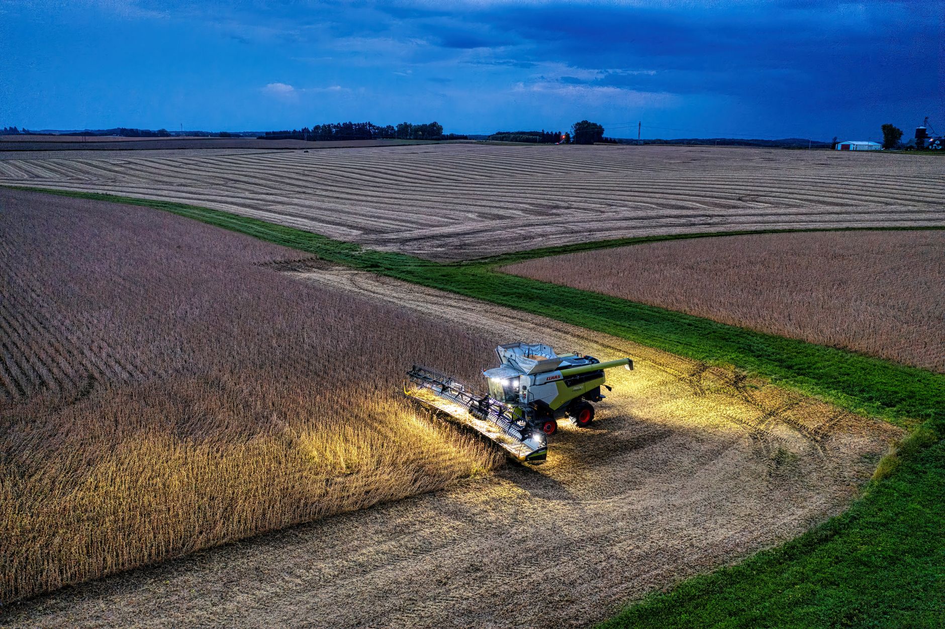 Drone captures a combine harvester working in Minnesota soybean fields at dusk.