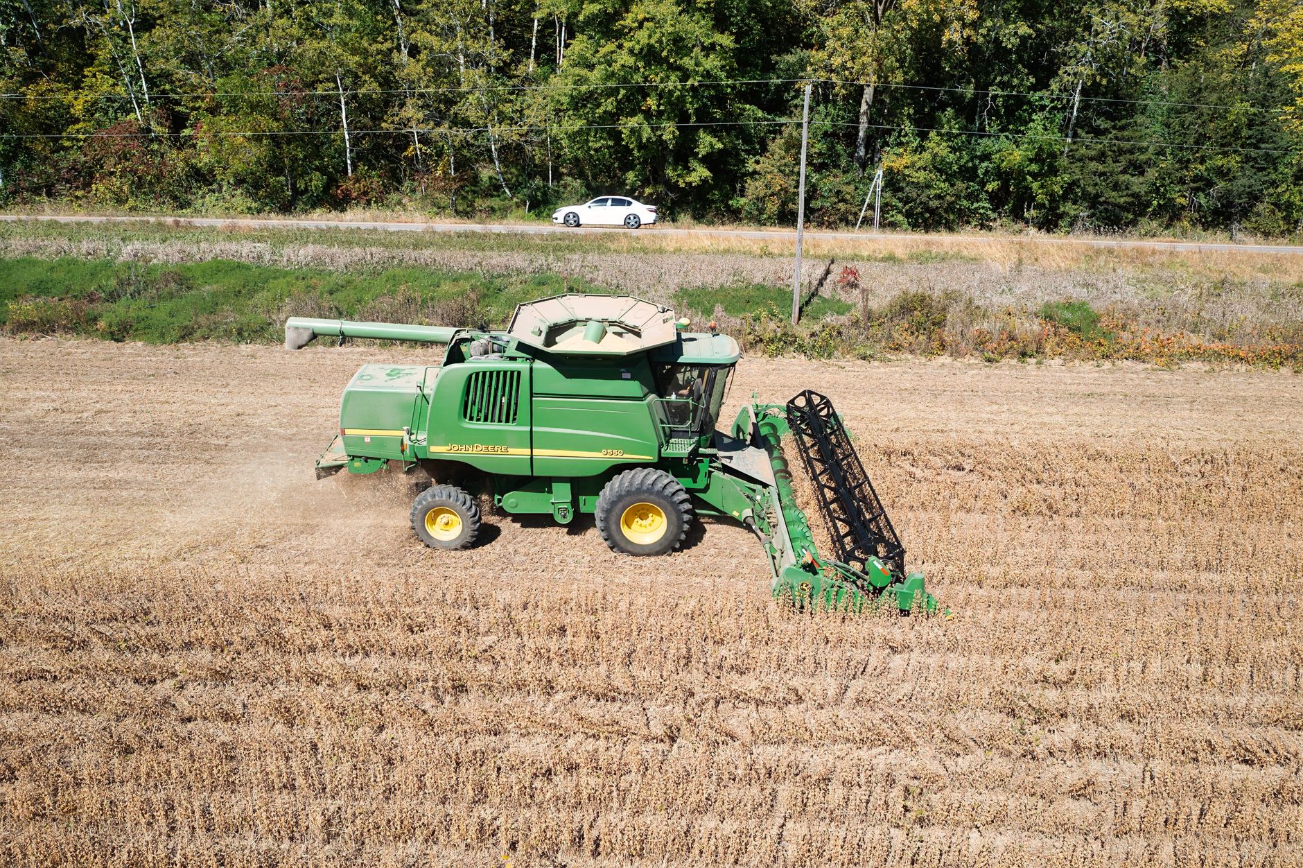 Aerial view of combine harvester in field with forest background in Minnesota.