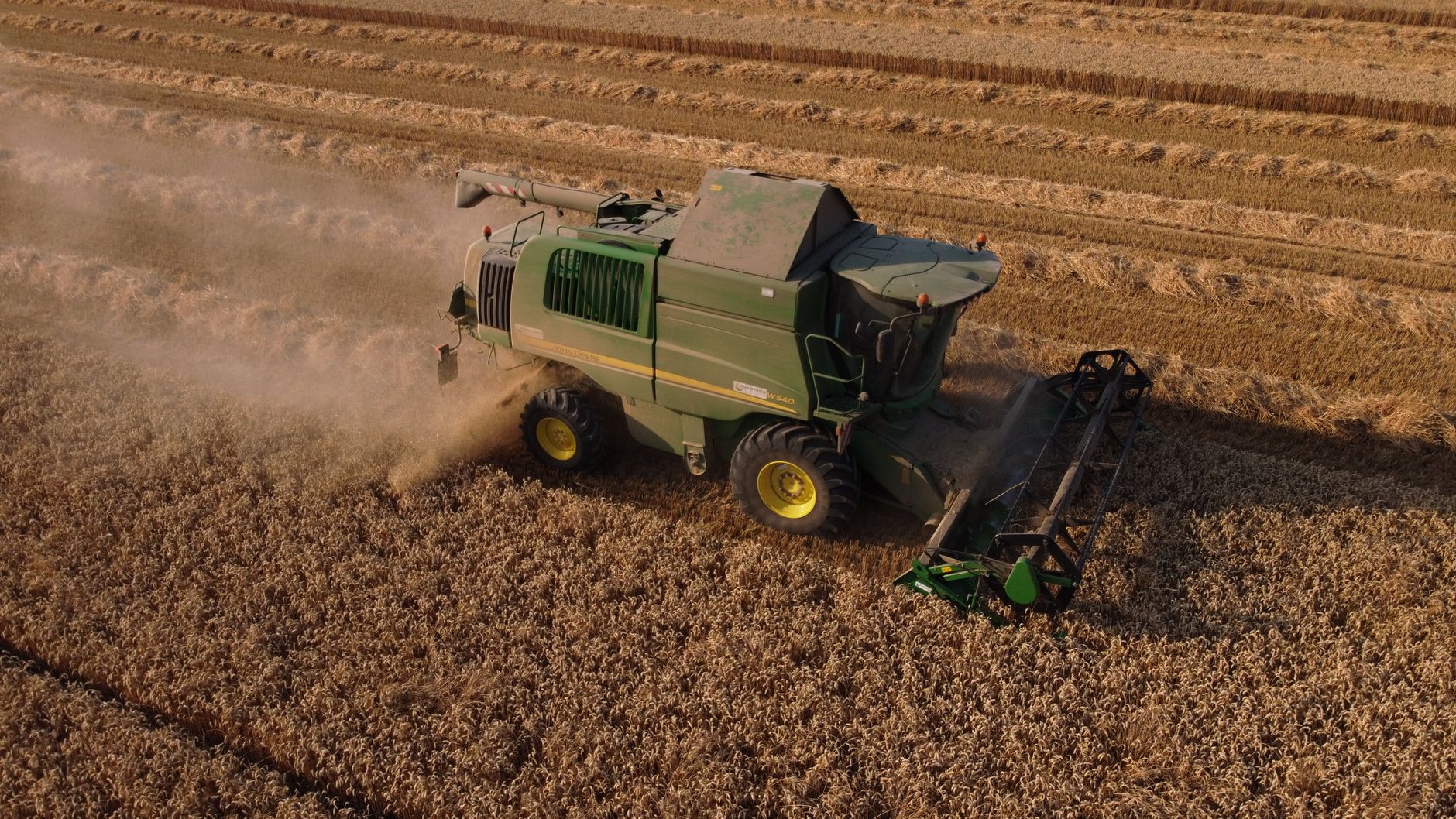 Aerial view of green combine harvester processing a wheat field in Saigneville, France, during harvest season.