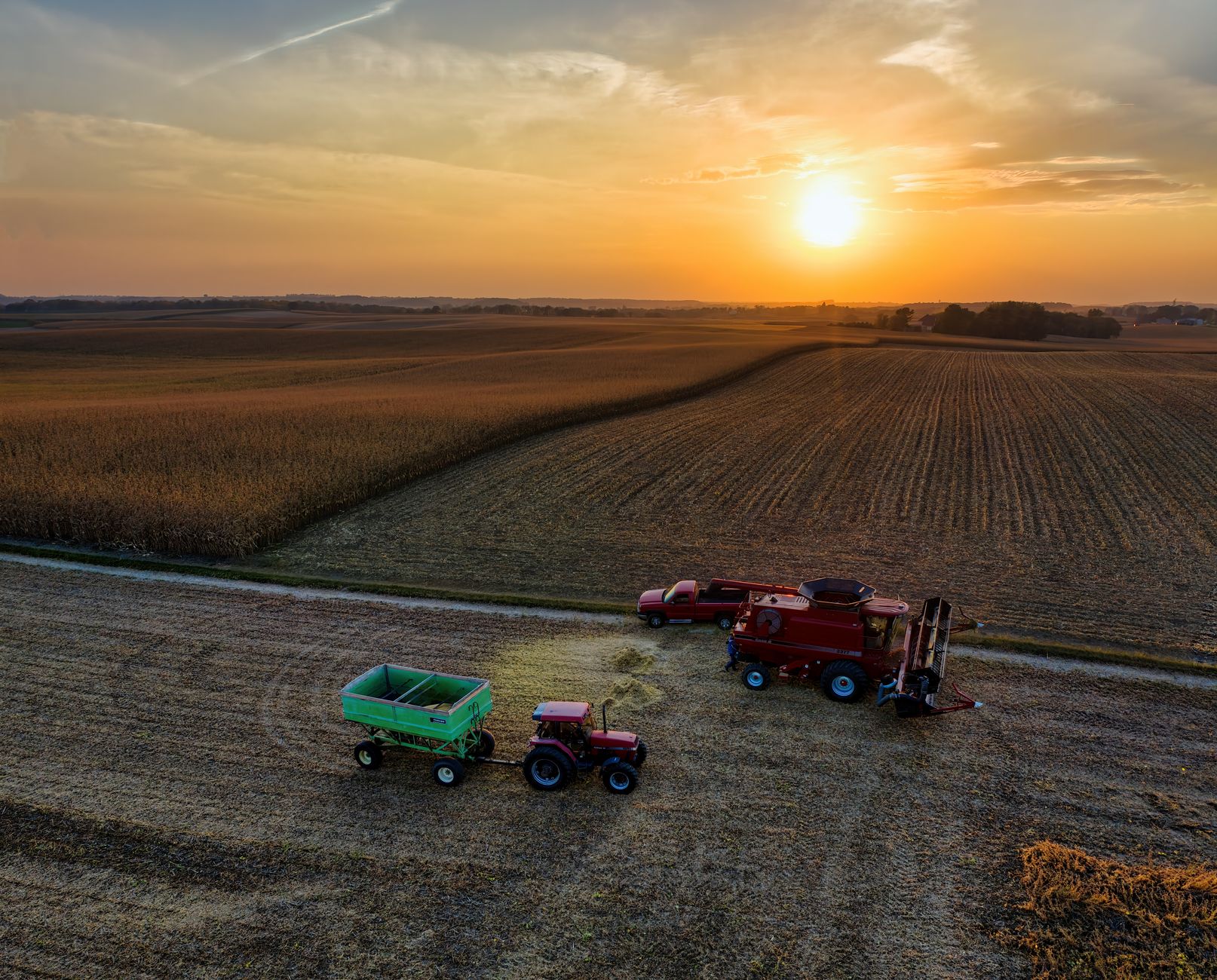 Drone shot capturing tractors and combine harvester working on a farm in Minnesota at sunset. Picturesque agricultural scene.