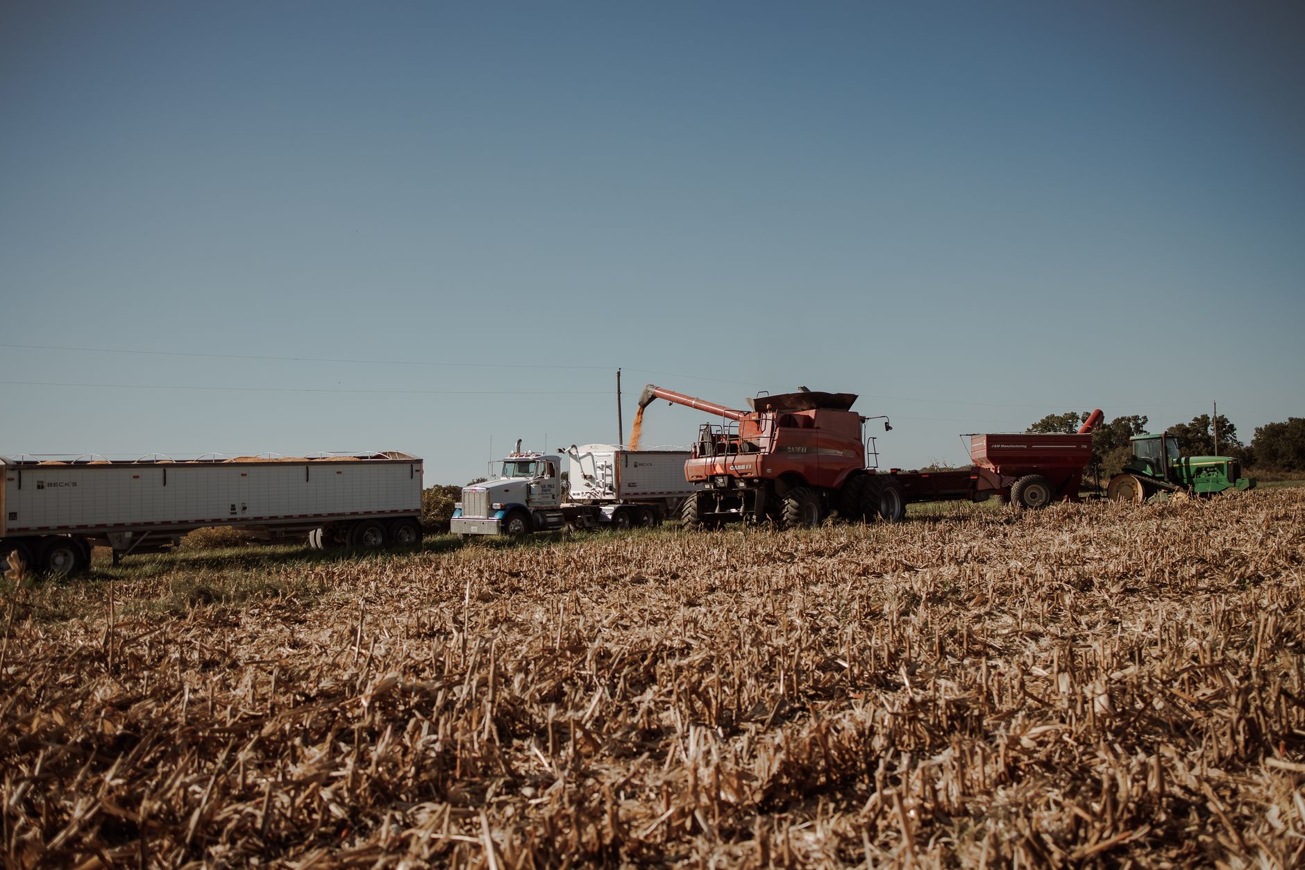 Tractors and harvesters working in a sunlit cropland during harvest season.