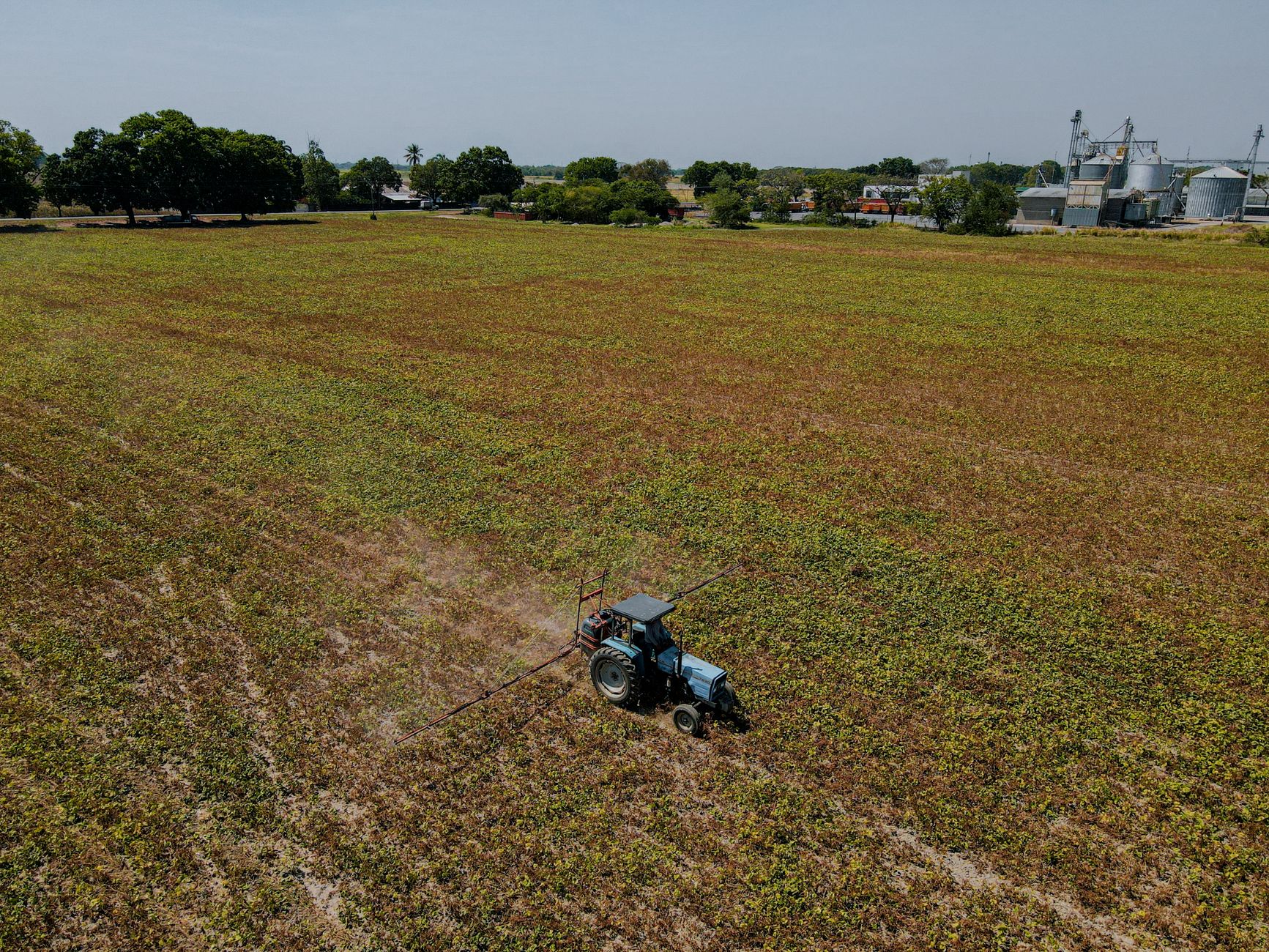Aerial view of a tractor operating in a large farmland under a clear sky, highlighting agricultural activity.