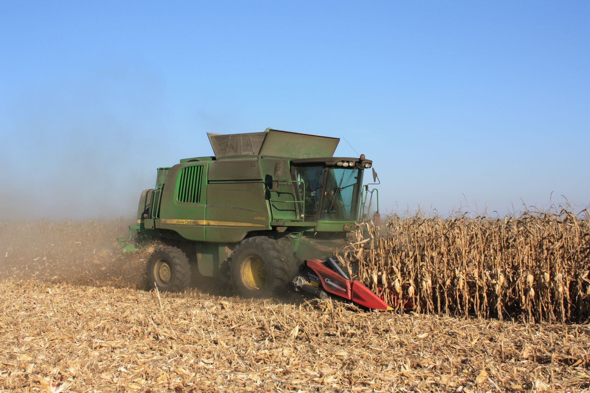Combine harvester in action during corn harvest on a sunny day showing modern agriculture machinery.