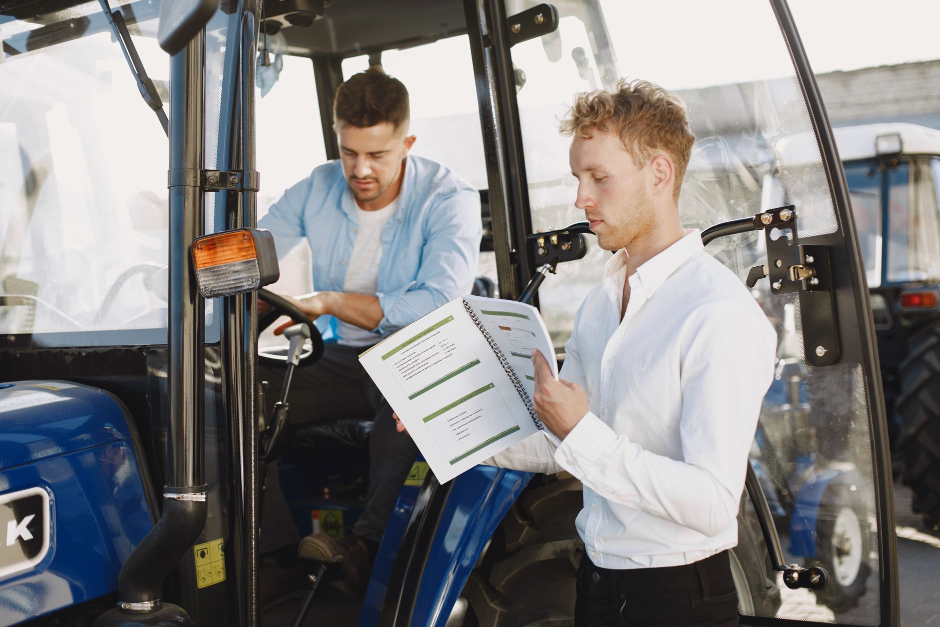 Two men reviewing documents near farm machinery, highlighting agricultural operation.
