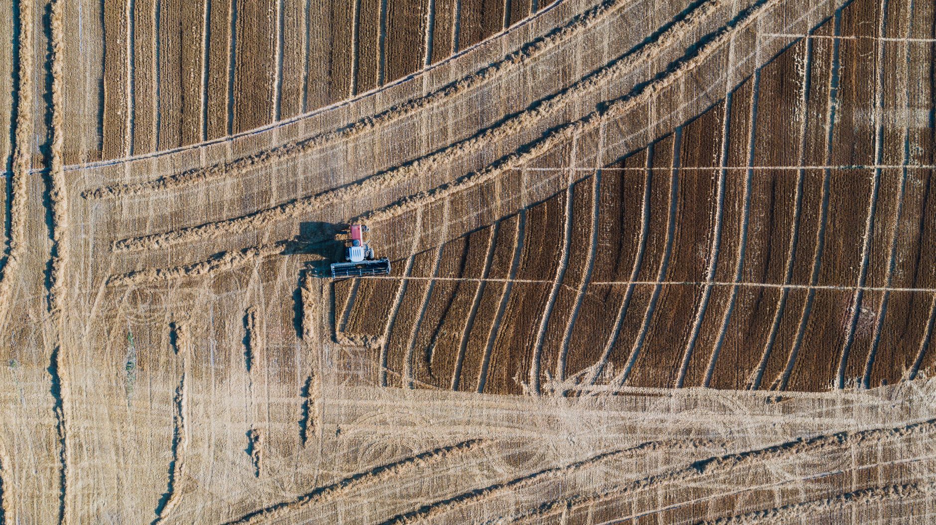 Drone shot capturing a tractor plowing agricultural fields in a geometric pattern.