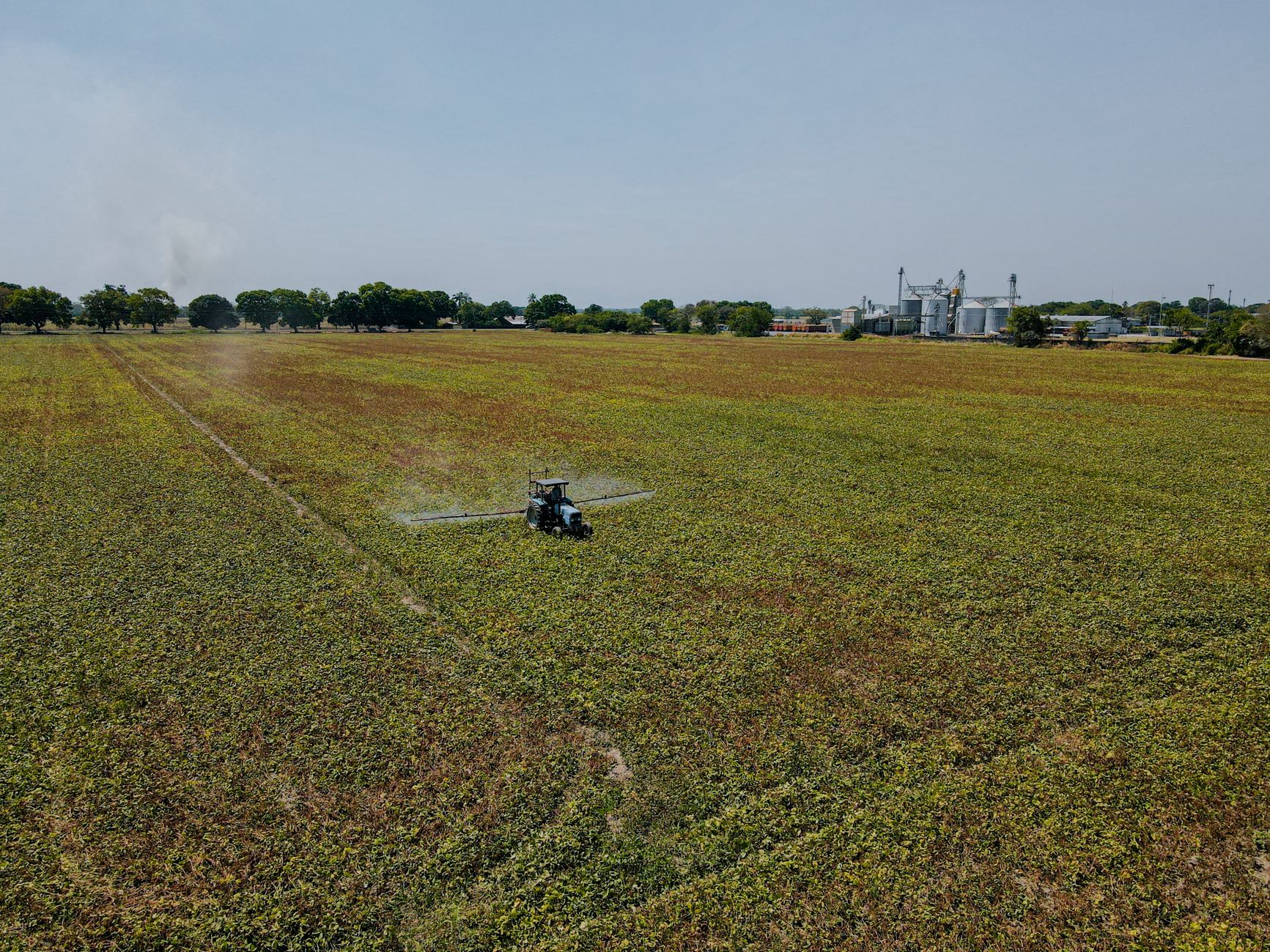 An expansive aerial view of a tractor working in a vast agricultural field on a clear day.