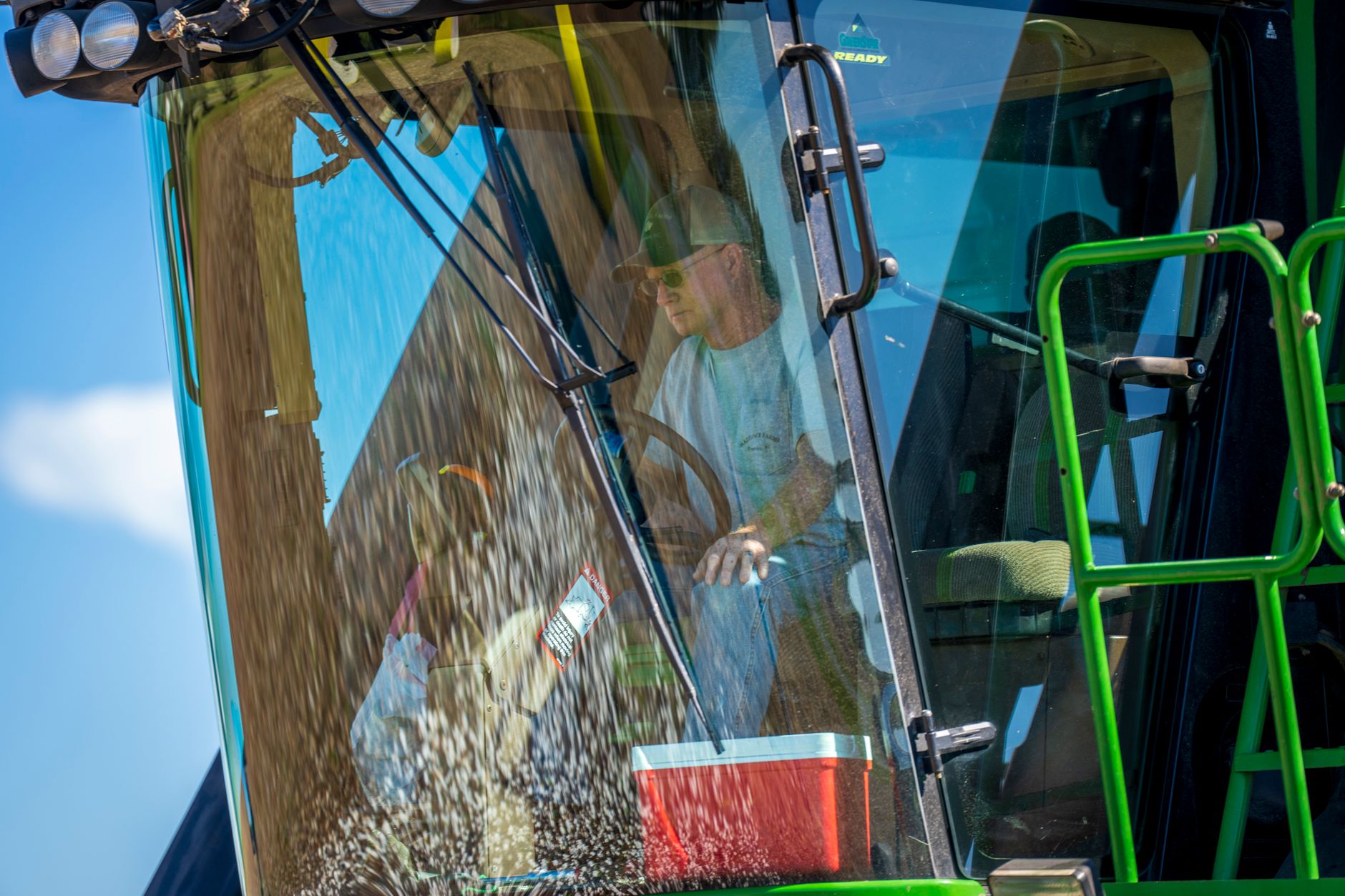 A man operating a green combine harvester in a sunny field, focusing on grain harvest.