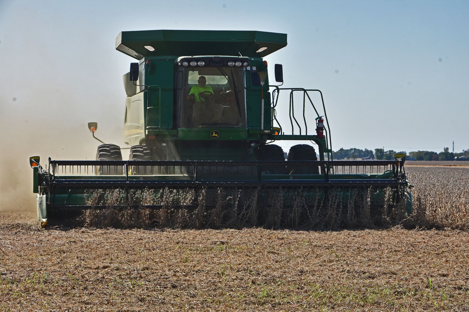 A combine harvester working in a field under clear blue sky during fall harvest.