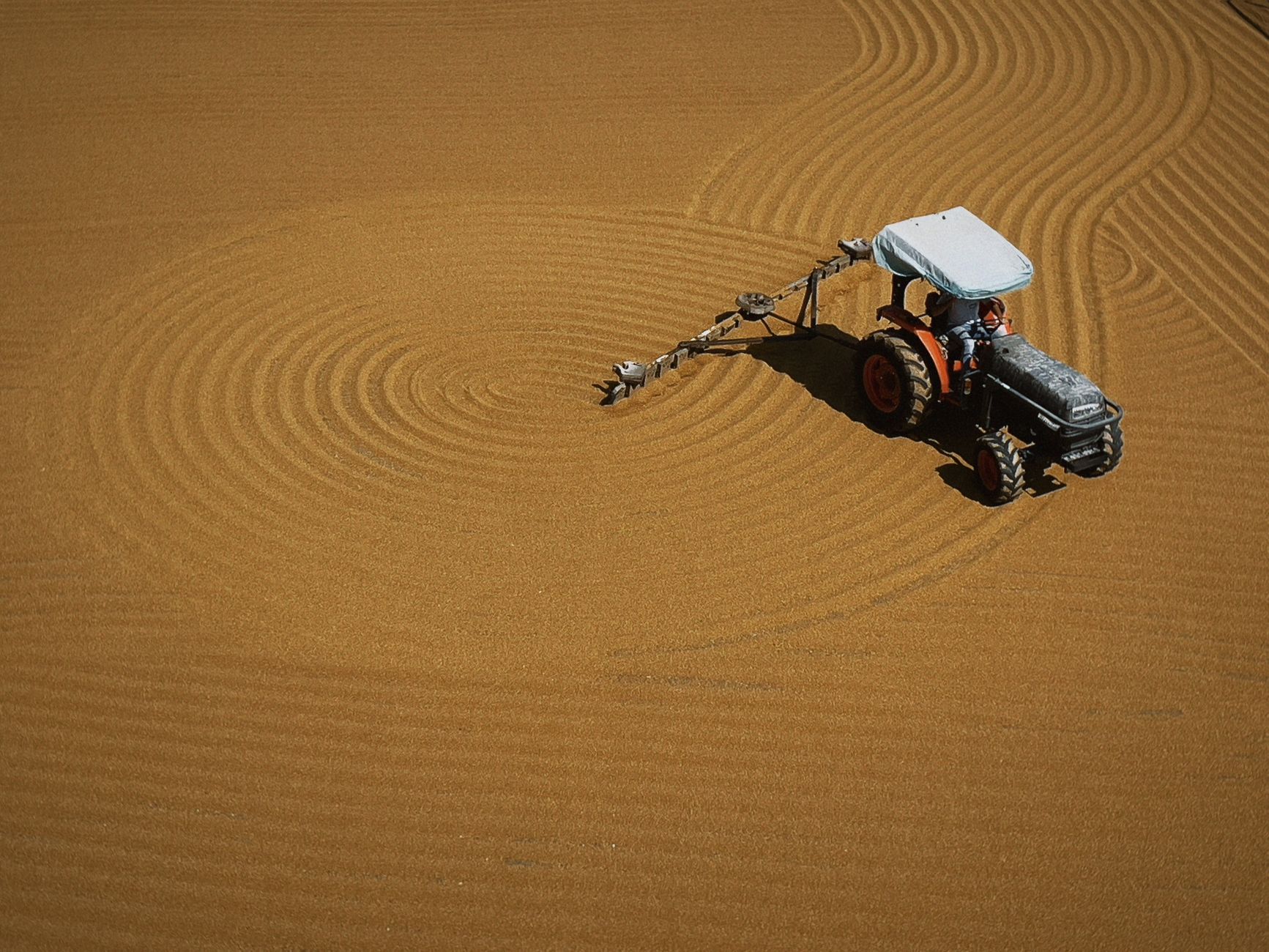 A tractor plows circular patterns in a field, captured from above.