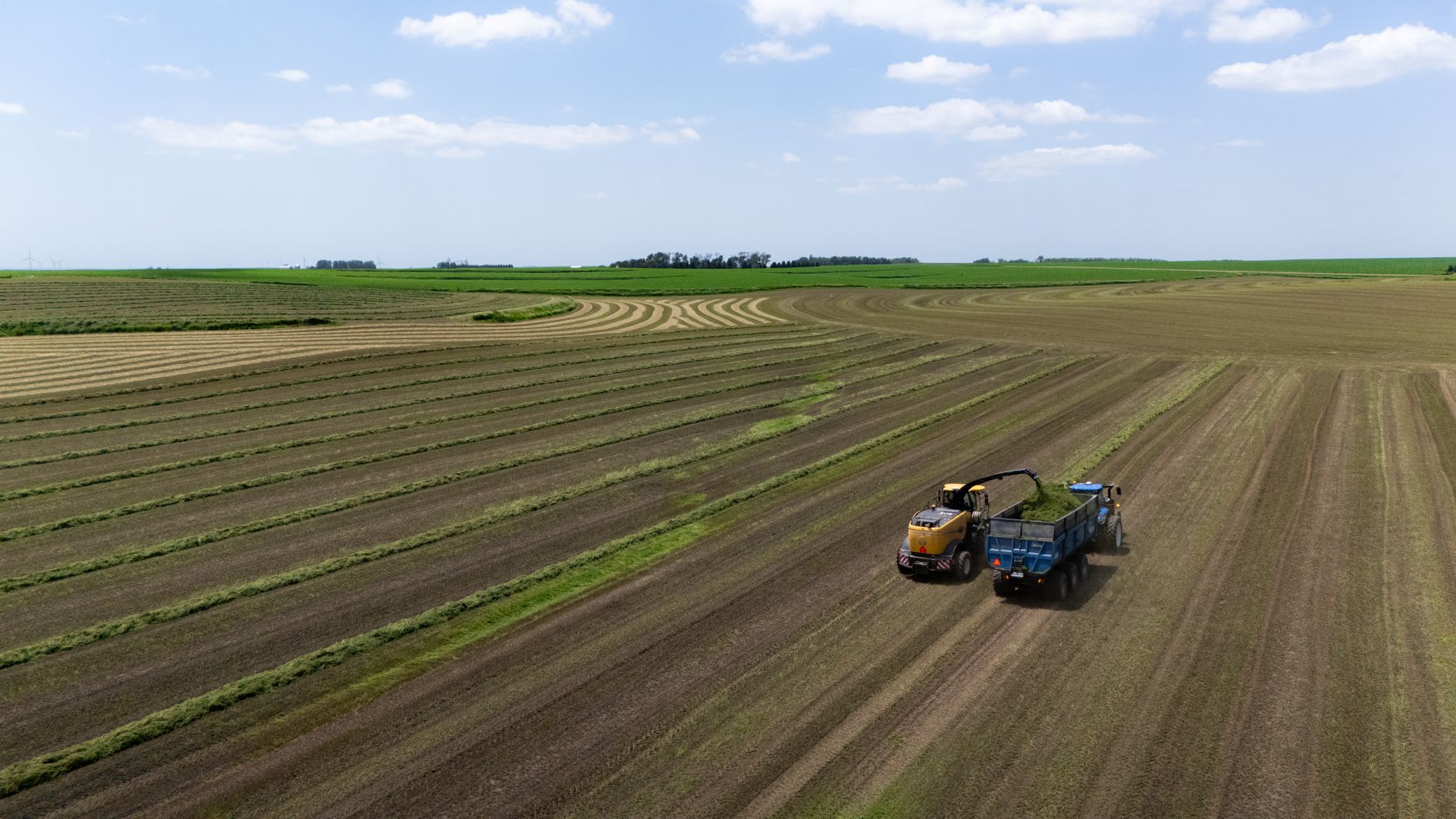 Aerial view of tractor harvesting crops in expansive farm fields under a clear sky.