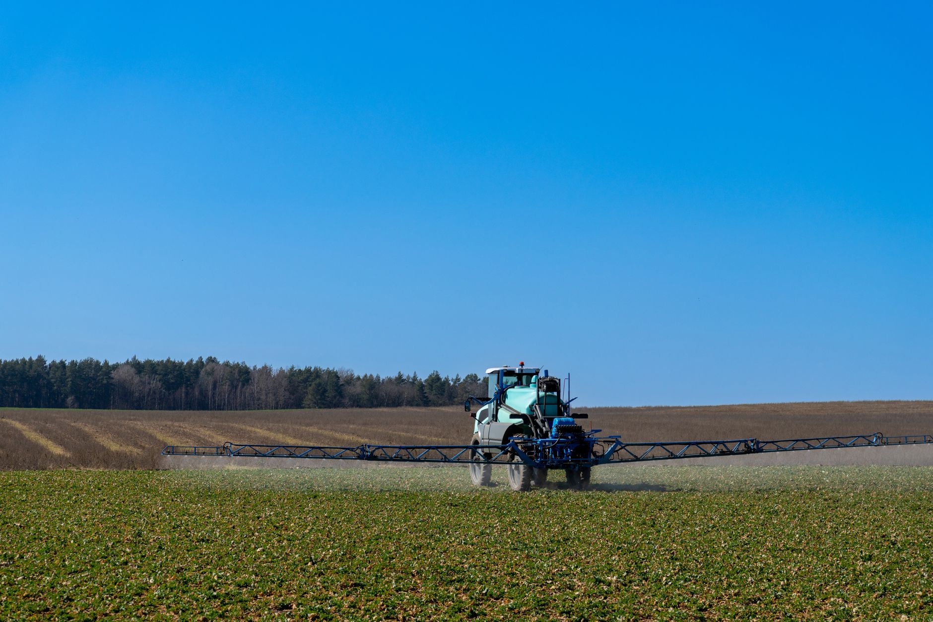 A tractor with spraying equipment fertilizing crops on a sunny day.