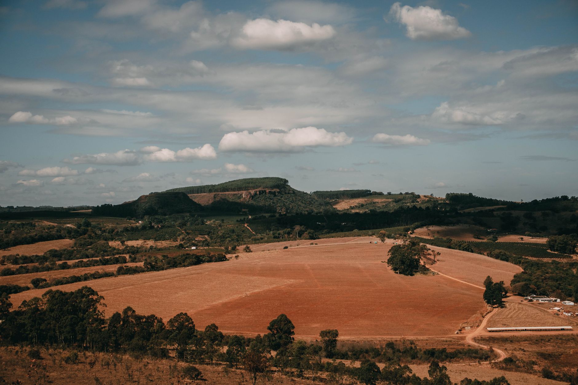 A panoramic aerial shot of a vast rural landscape with hills and trees under a cloudy sky.