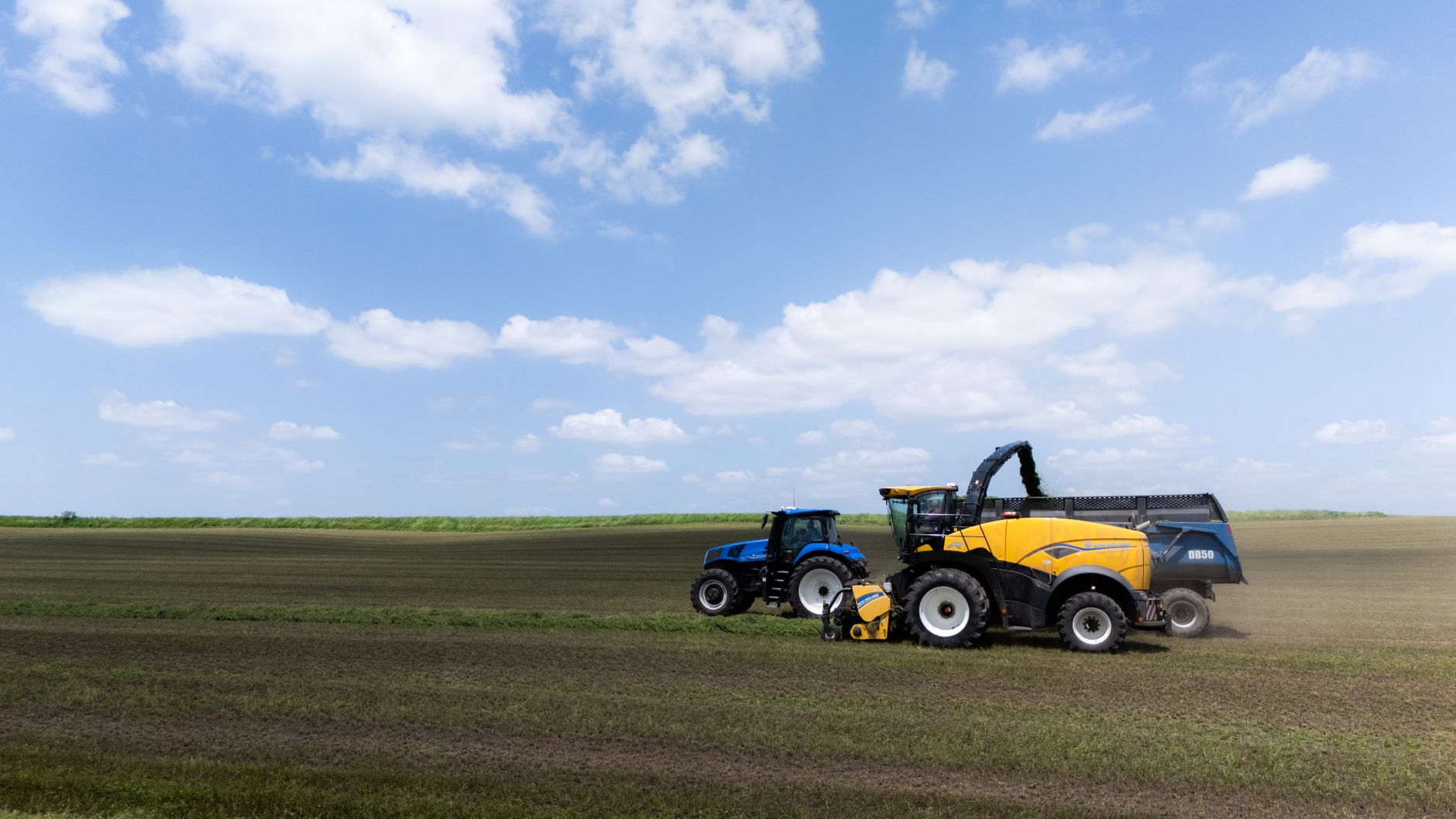 Two tractors working together in a vast field under a clear blue sky, harvesting crops efficiently.