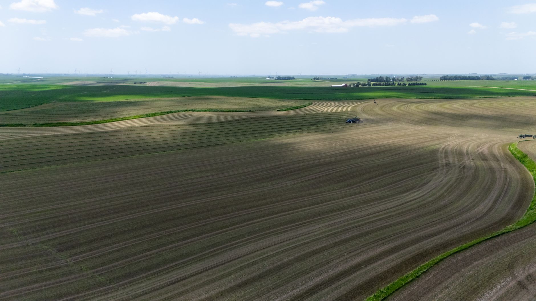 Beautiful aerial shot of farmland with tractors harvesting silage under a clear blue sky.