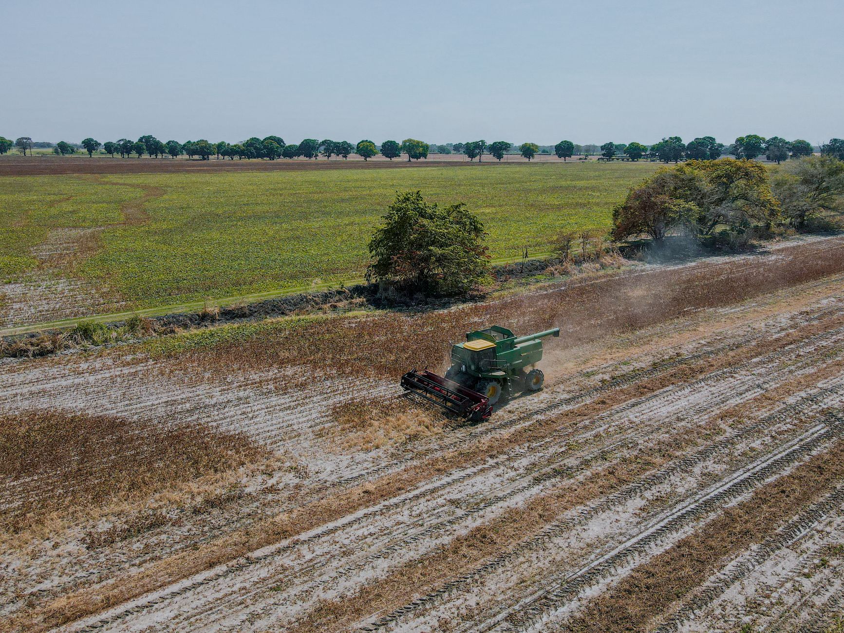 A combine harvester at work in a large agricultural field, captured from above during the day.