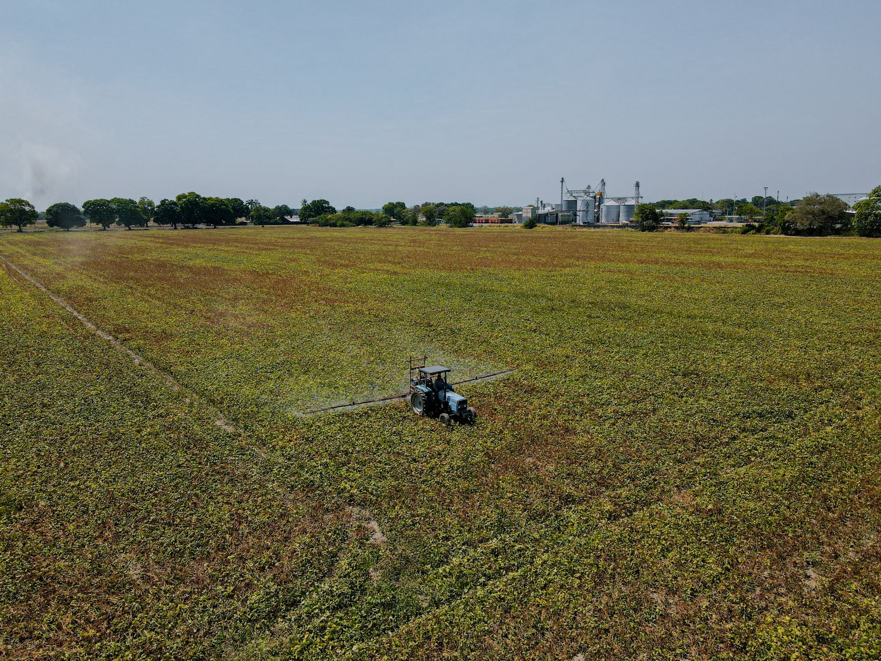 Aerial shot of a tractor spraying crops in an expansive agricultural field during the day.