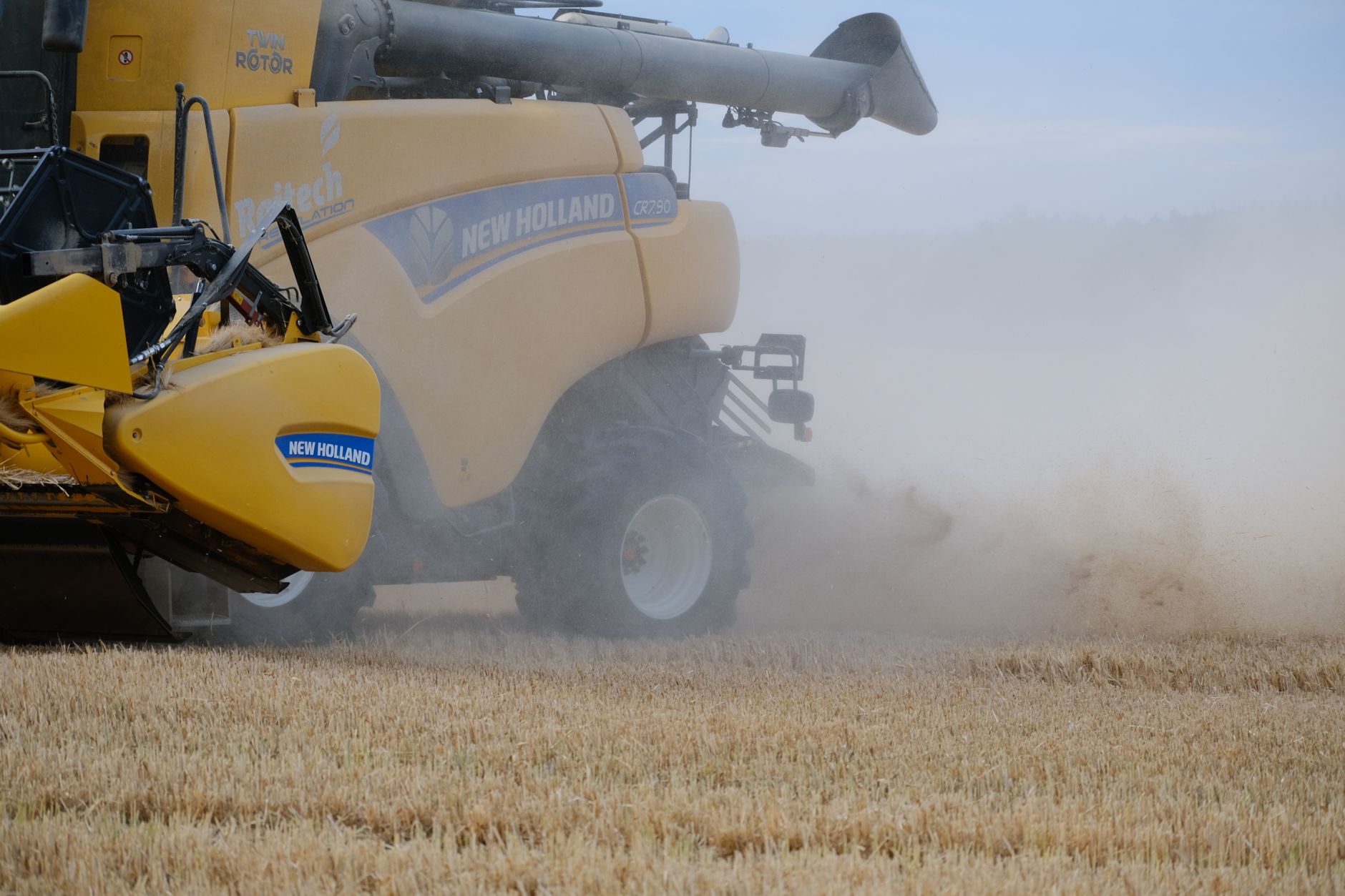 A yellow harvester working through a wheat field creating dust during daytime harvesting activities.