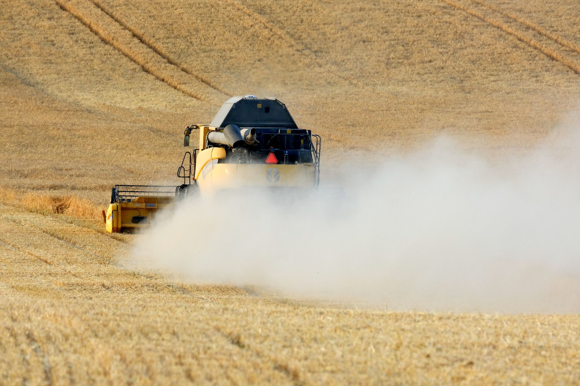 Combine harvester working tirelessly in a dusty golden field during harvest season.