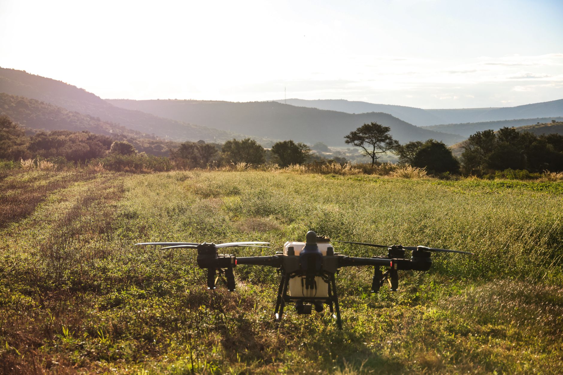 A drone ready for takeoff on a scenic agricultural field, capturing a beautiful sunrise.