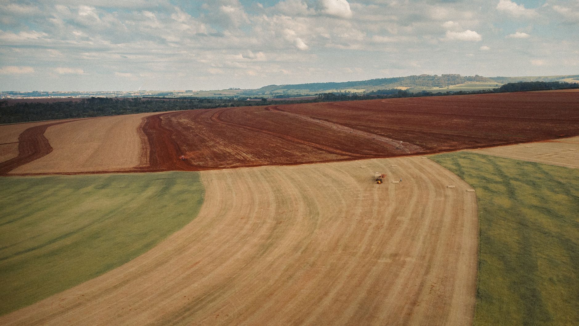 Aerial view of expansive cultivated fields with a tractor in rural countryside.