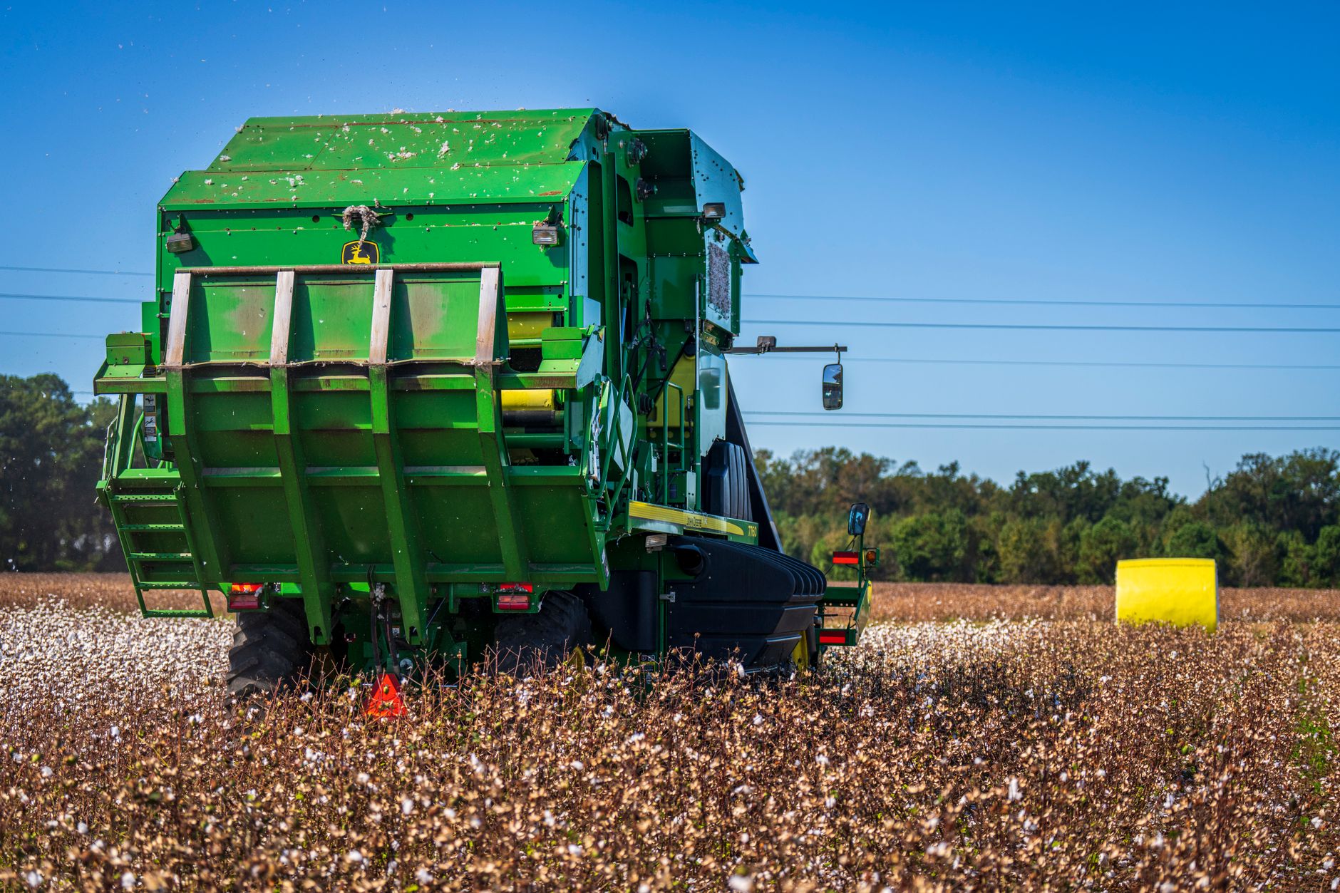Cotton harvesting in a field using a green tractor during a bright day.