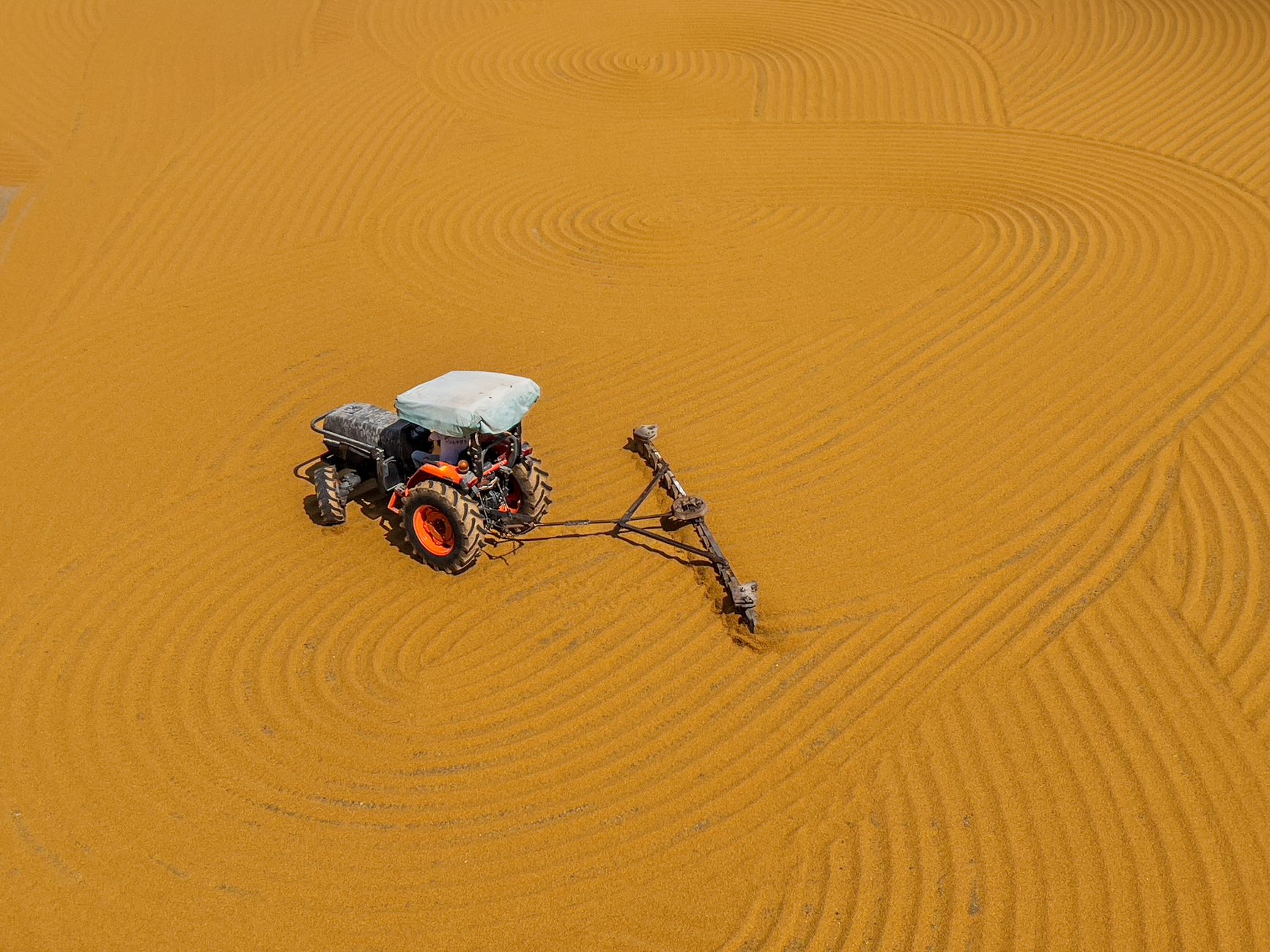 A solitary tractor creating intricate patterns in a vast yellow field from high above.